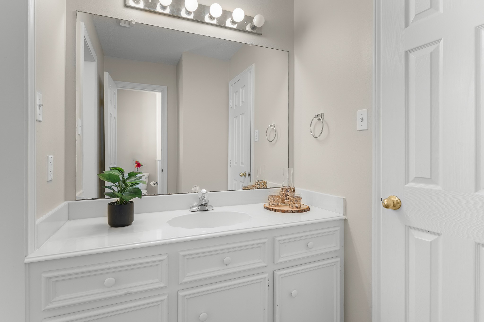 Classic white cabinetry, a broad mirror and bright vanity lighting keep the bathroom feeling fresh and functional.