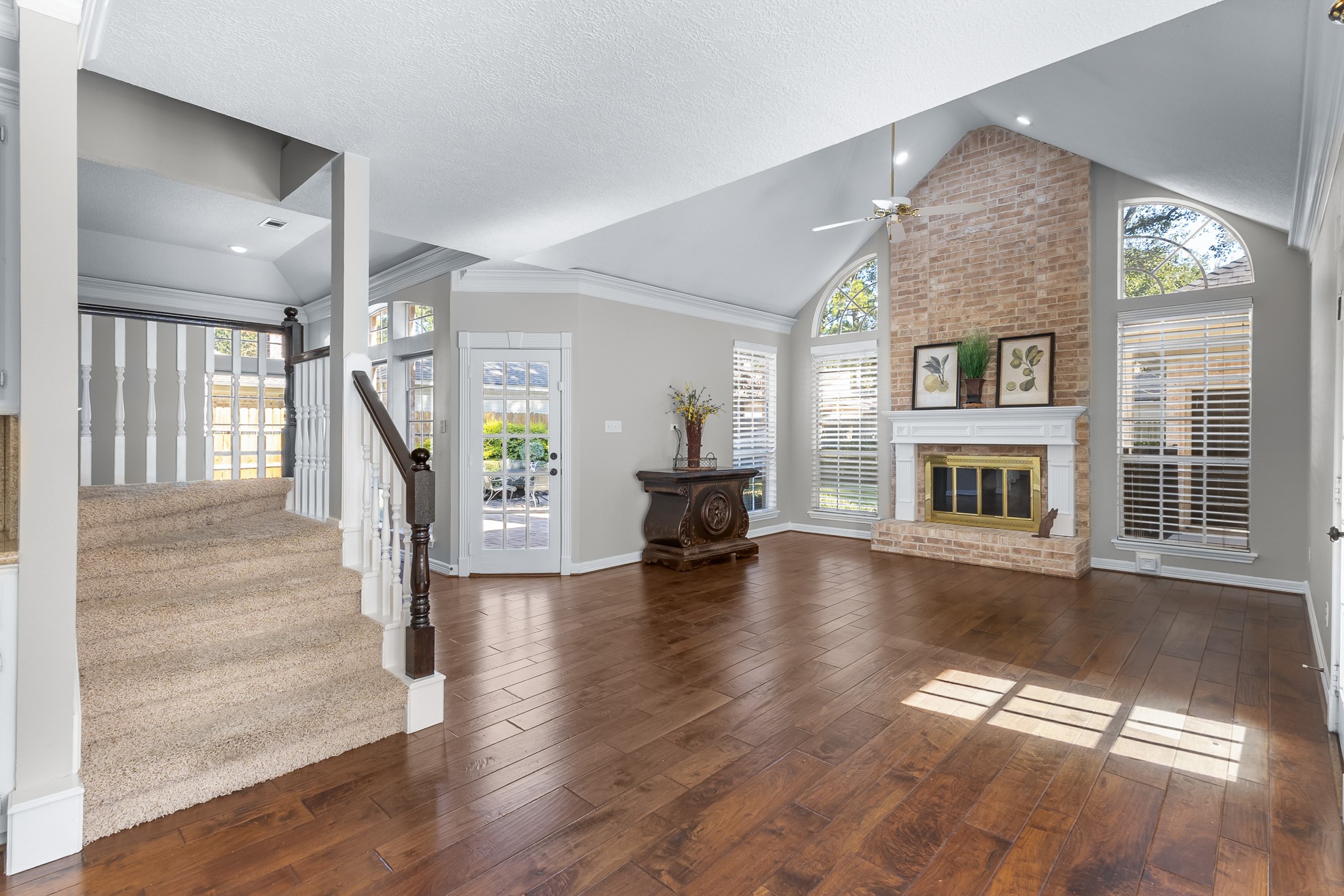 A dramatic brick fireplace rises between expansive windows, anchoring the family room beneath its vaulted ceiling.