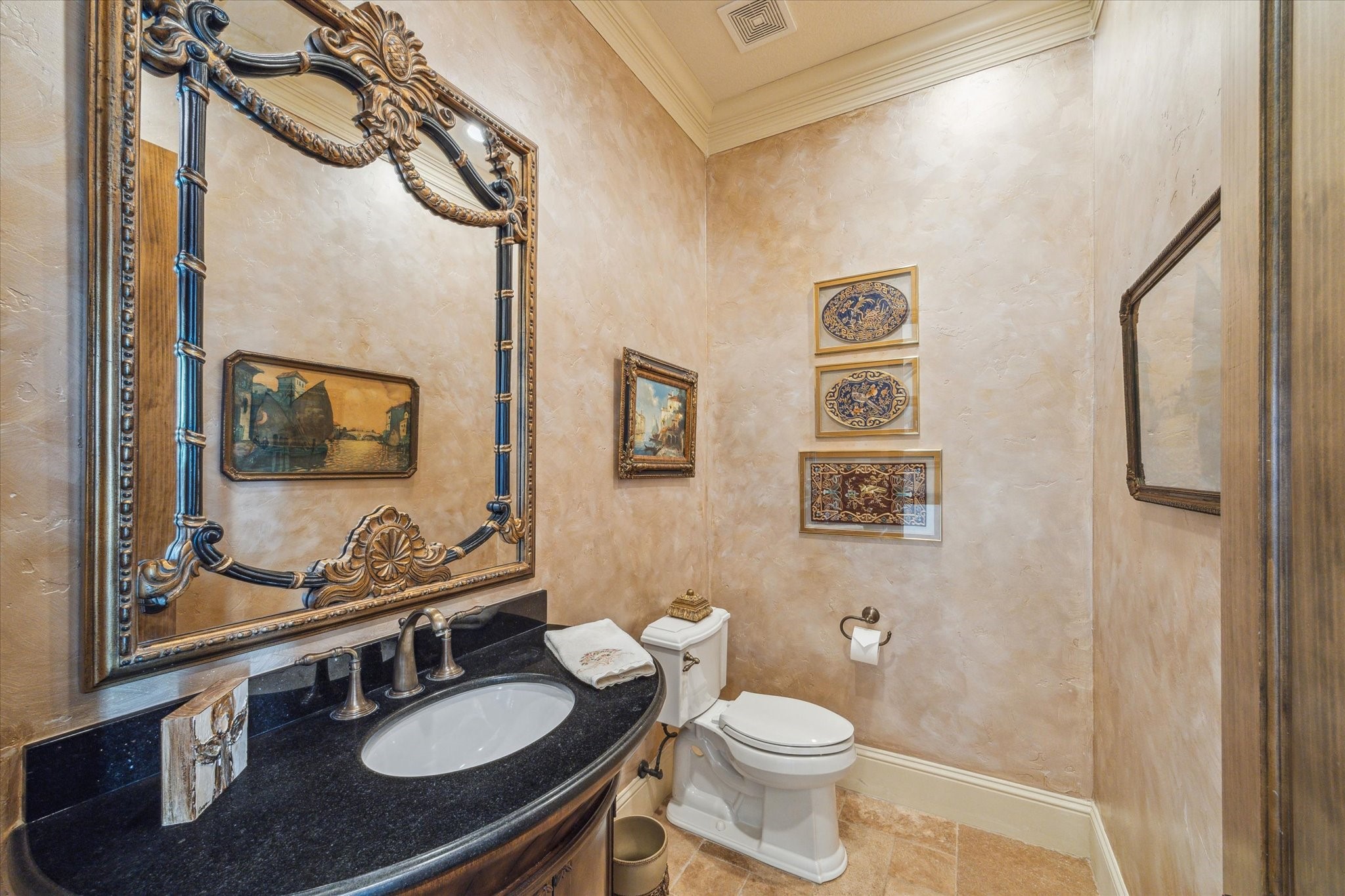 The powder room offers added convenience for guests, featuring rich textured walls, elegant crown molding, and a granite-topped vanity with warm wood cabinetry. A decorative framed mirror and ambient lighting completing the space