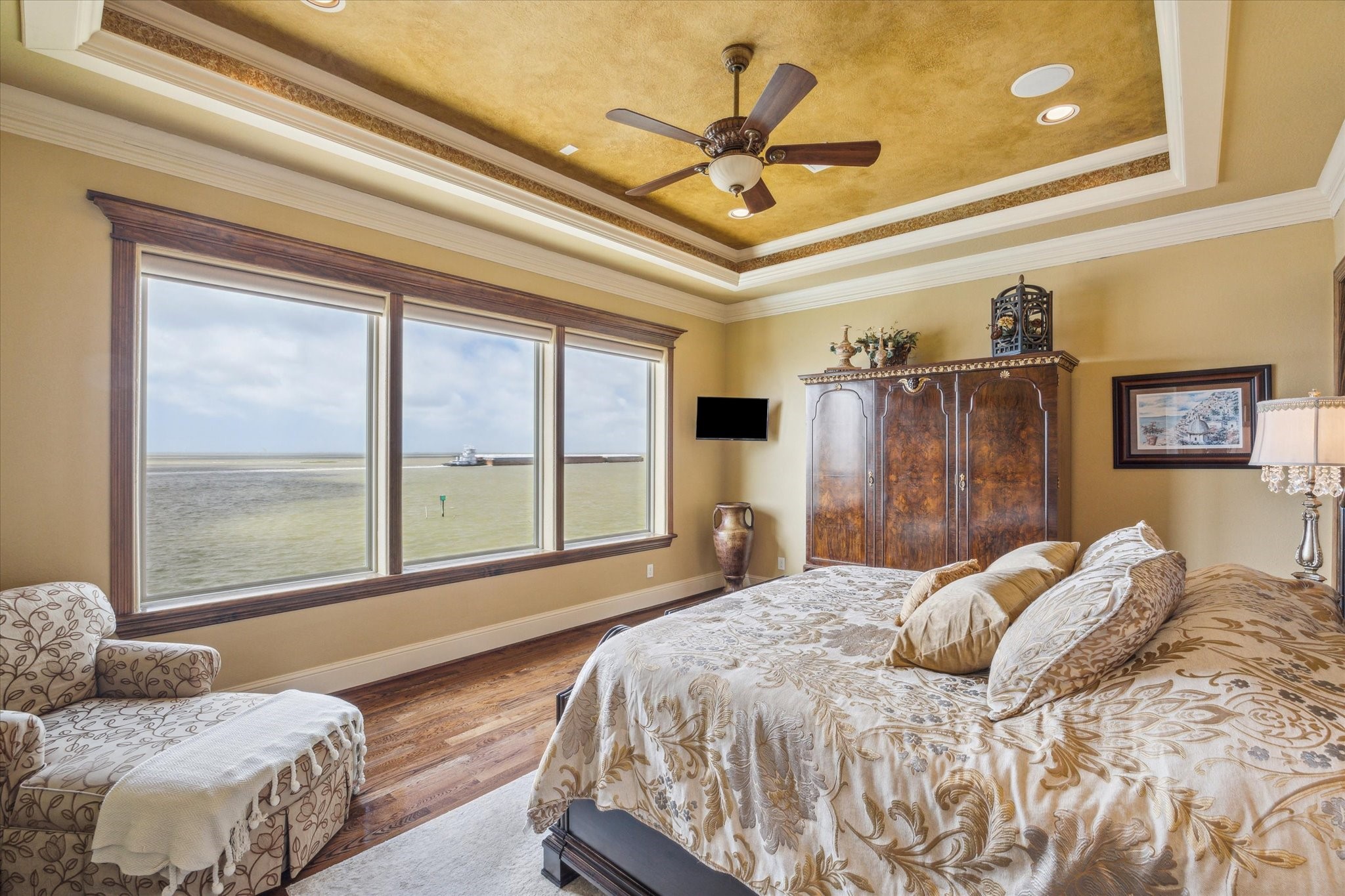 The primary suite features expansive windows with remote-control blinds, framing truly inspirational views of West Galveston Bay. A recessed ceiling adds a touch of architectural elegance, enhancing the rooms serene and sophisticated ambiance
