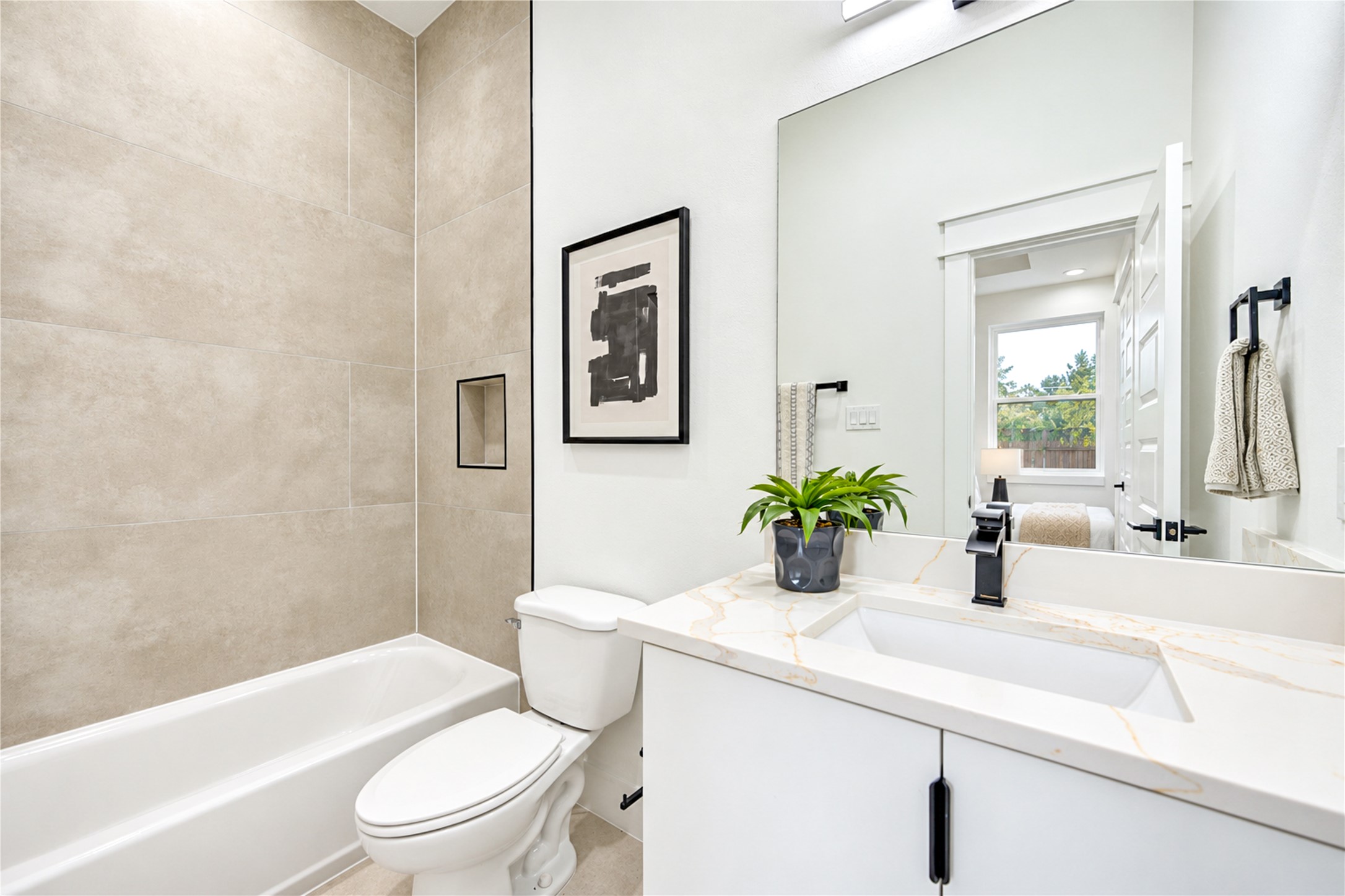 Convenient first-floor ensuite full bath showcasing a modern single vanity with quartz counters, sleek matte black hardware, and a tub/shower combo with large-format neutral tile.