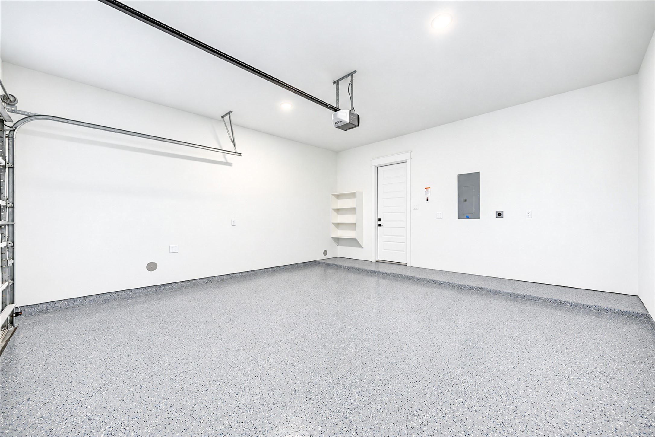 Pristine garage space featuring a durable grey epoxy floor coating, custom built-in shelving, bright recessed lighting, and direct interior access.