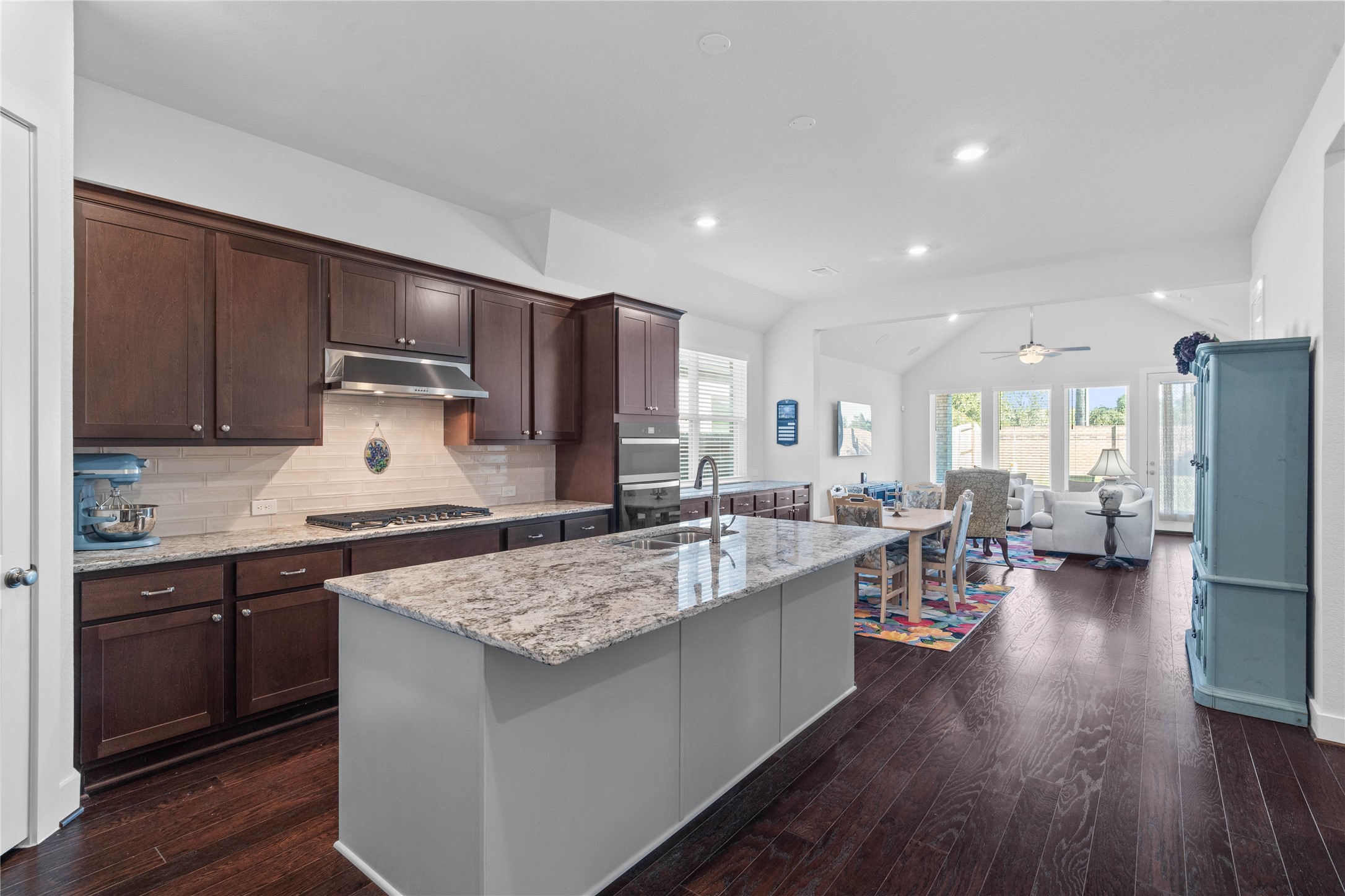 The chefs kitchen serves as the heart of the home, featuring rich dark cabinetry, built-in stainless steel appliances, a modern backsplash, and a spacious center island with a granite countertop that flows seamlessly into the open-concept dining and living areas.