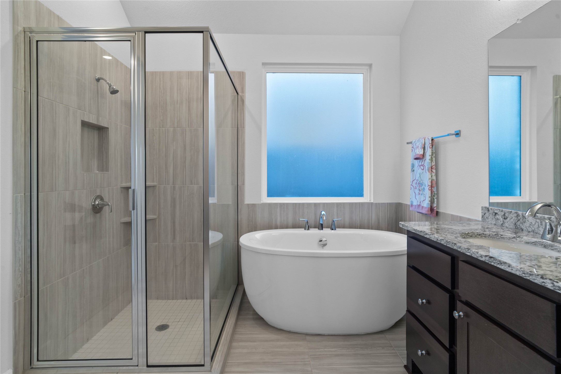 A closer look at the spa-inspired amenities, highlighting the deep freestanding soaking tub positioned beneath a large frosted privacy window, alongside a separate glass-enclosed walk-in shower complete with floor-to-ceiling tile work and an integrated storage niche.