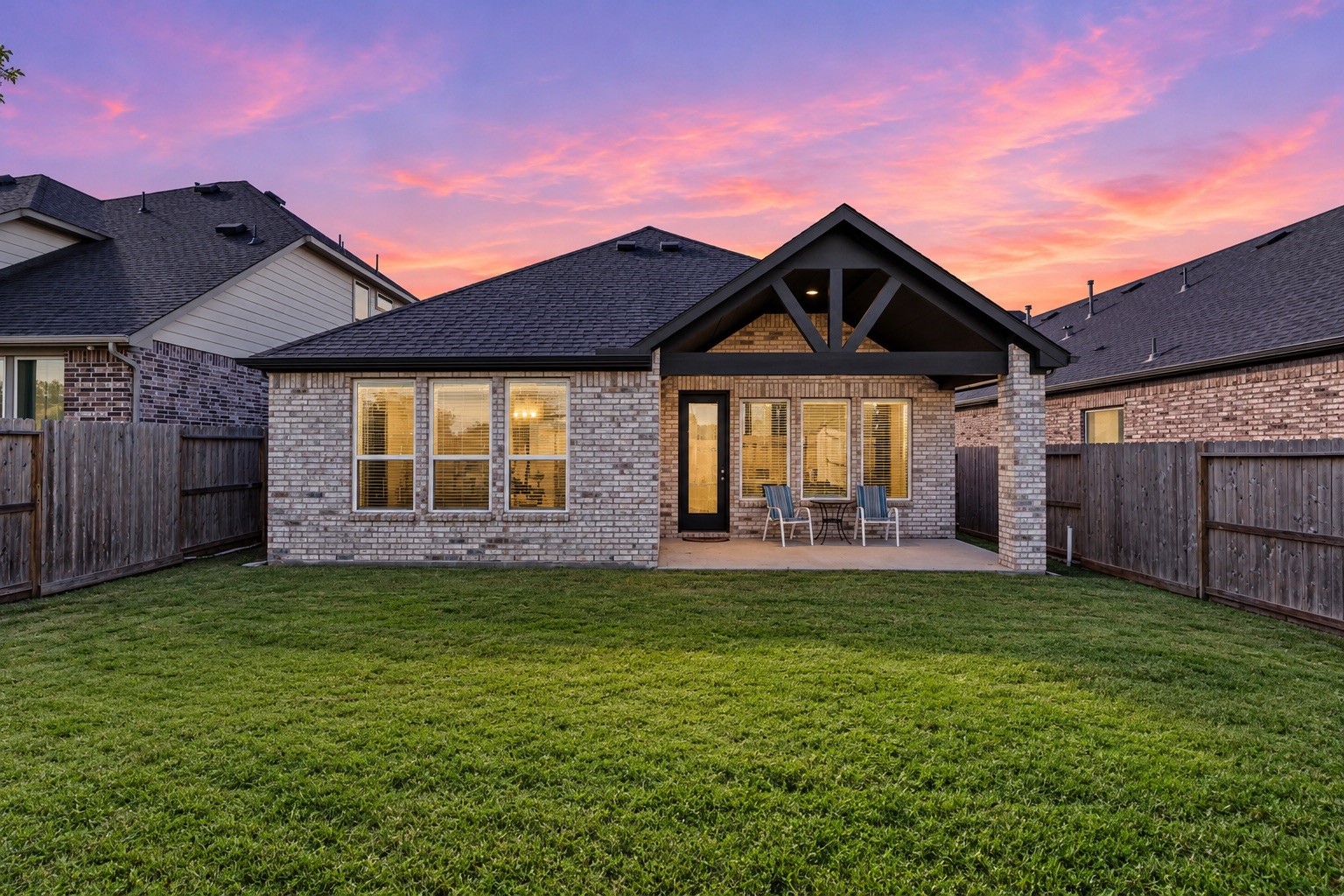 A full view of the home's rear exterior highlights the robust brick architecture, showcasing the spacious covered patio and expansive green lawn that perfectly sets the stage for memorable outdoor entertainment and peaceful relaxation.