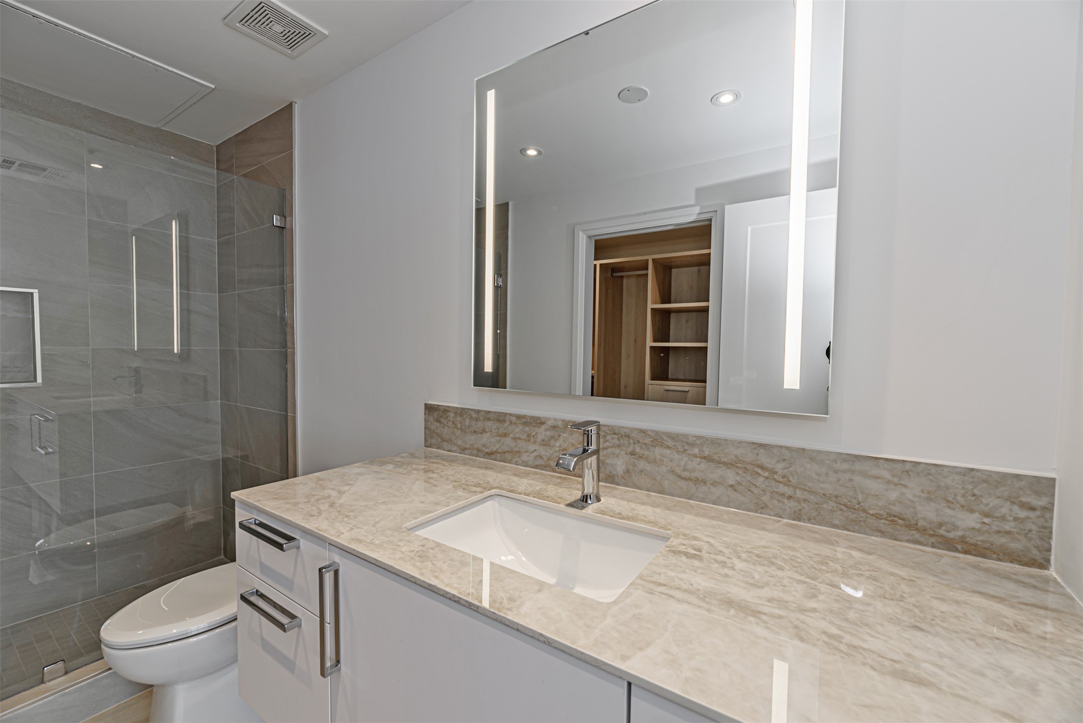 Designer finishes include backlit vanity mirror, porcelain countertop and frameless glass shower with hand-held sprayer.