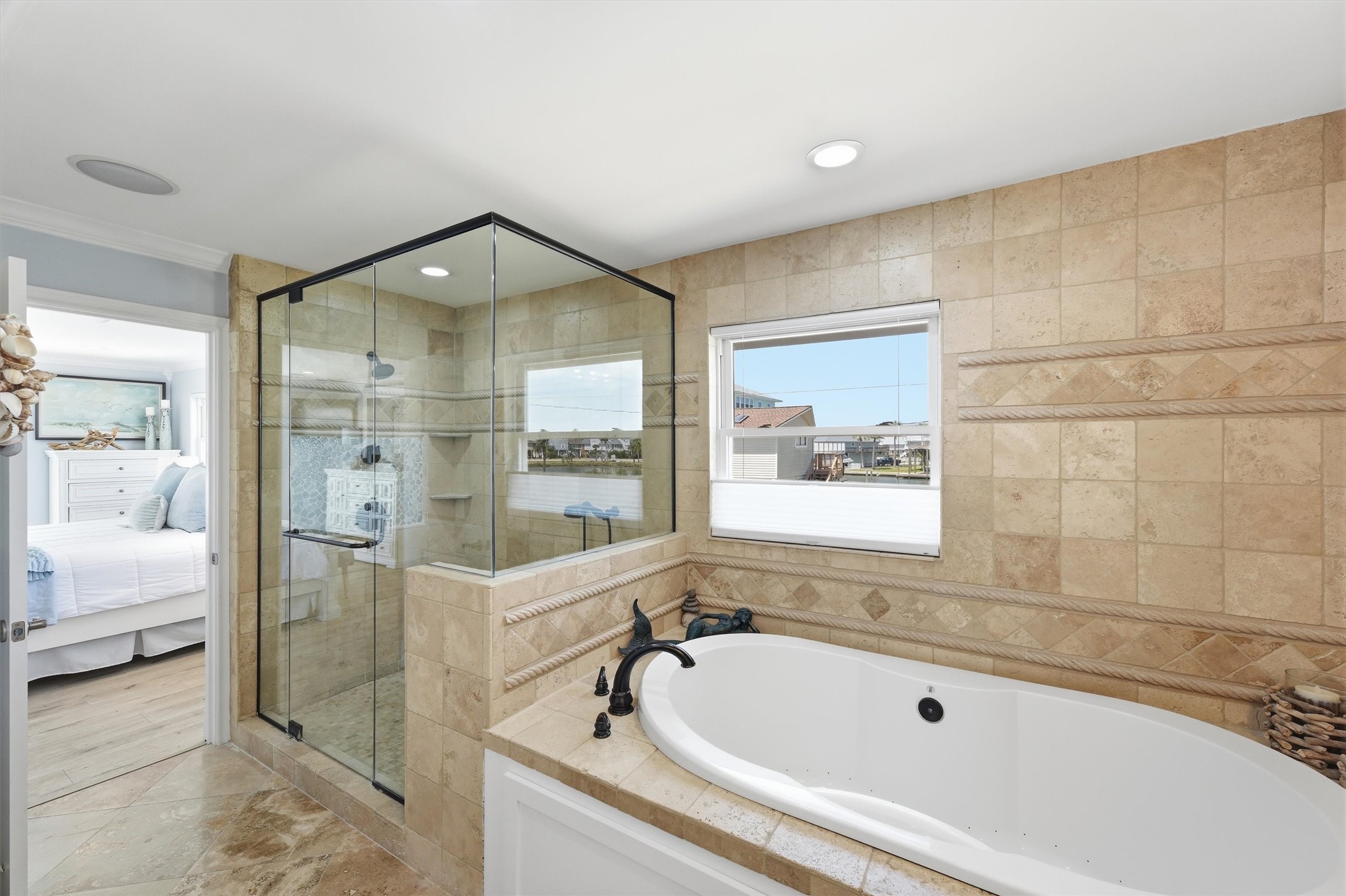 Primary bath offers a jetted soaking tub and oversized glass-enclosed shower surrounded by warm stone finishes.