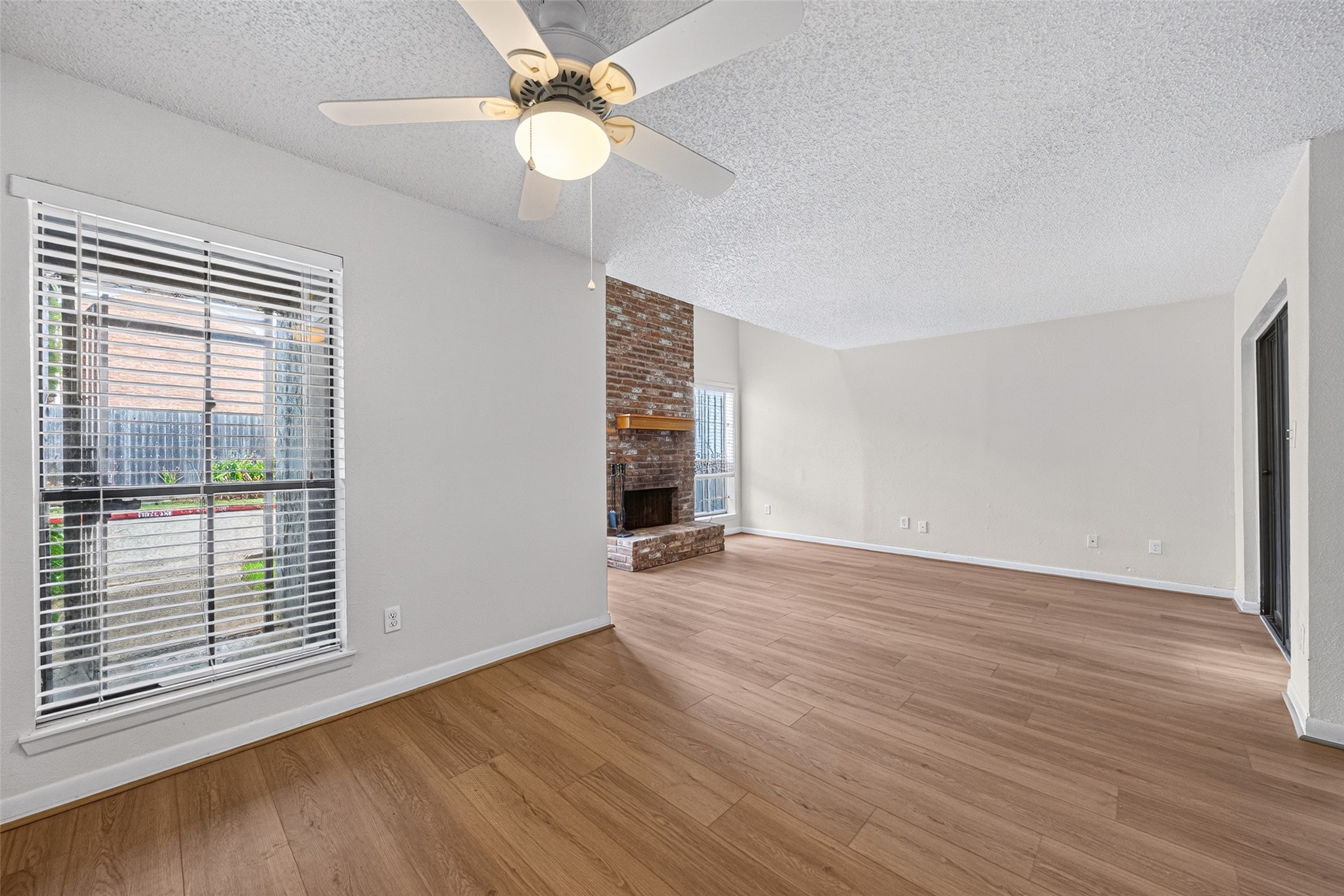 Open-concept living and dining areas with new vinyl flooring, abundant natural light, and a brick fireplace.