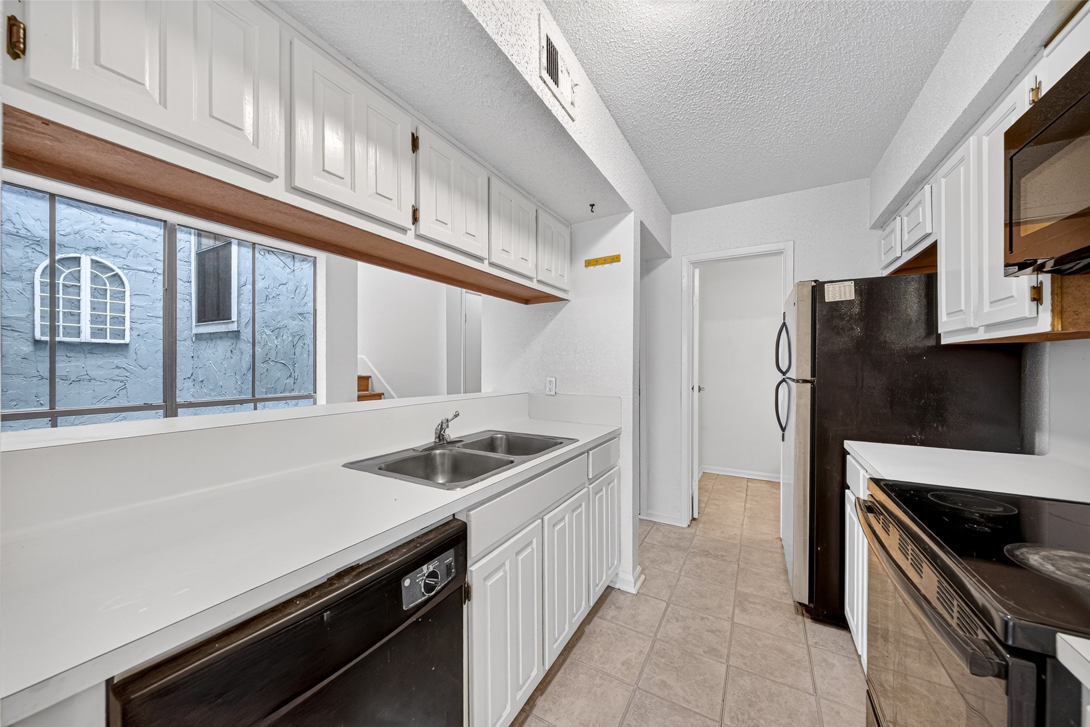 Functional kitchen featuring white cabinetry, breakfast bar, double-basin sink, and black appliances.