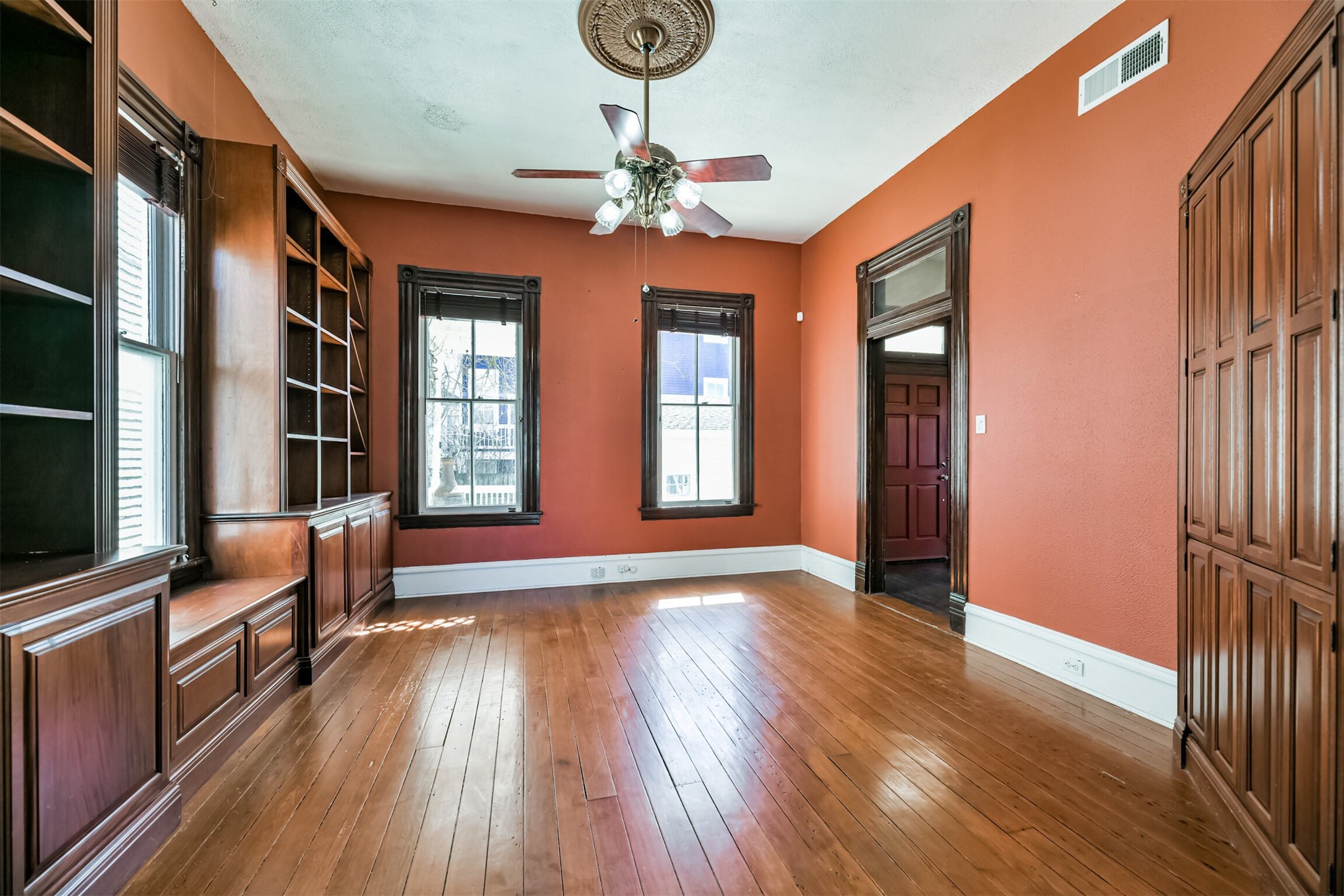 An alternate view of the family room highlights the handsome long leaf pine wood flooring, ornate ceiling medallion with a lighted fan suspended from it, and beautifully cased windows and doors with an original transom window above the door.