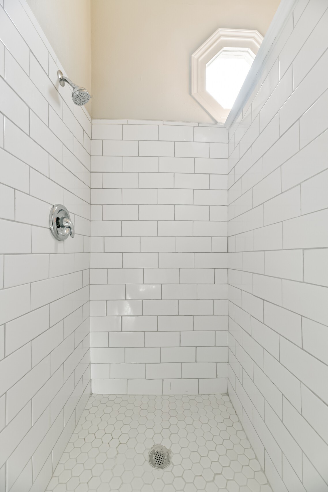 The walk-in shower showcases a timeless subway tile finish that complements the hexagonal tile floors. A window above adds natural light to this bathroom.