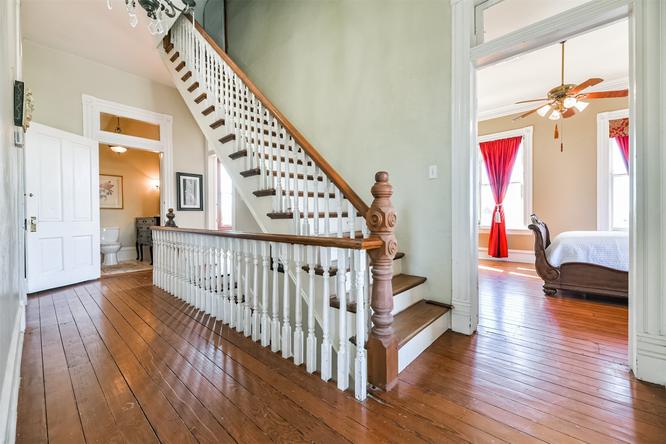 The original staircase with wood treads, white balusters, and ornately carved newel posts leads up from the foyer to this second-floor landing that hosts long leaf pine floors along with three bedrooms and two bathrooms.