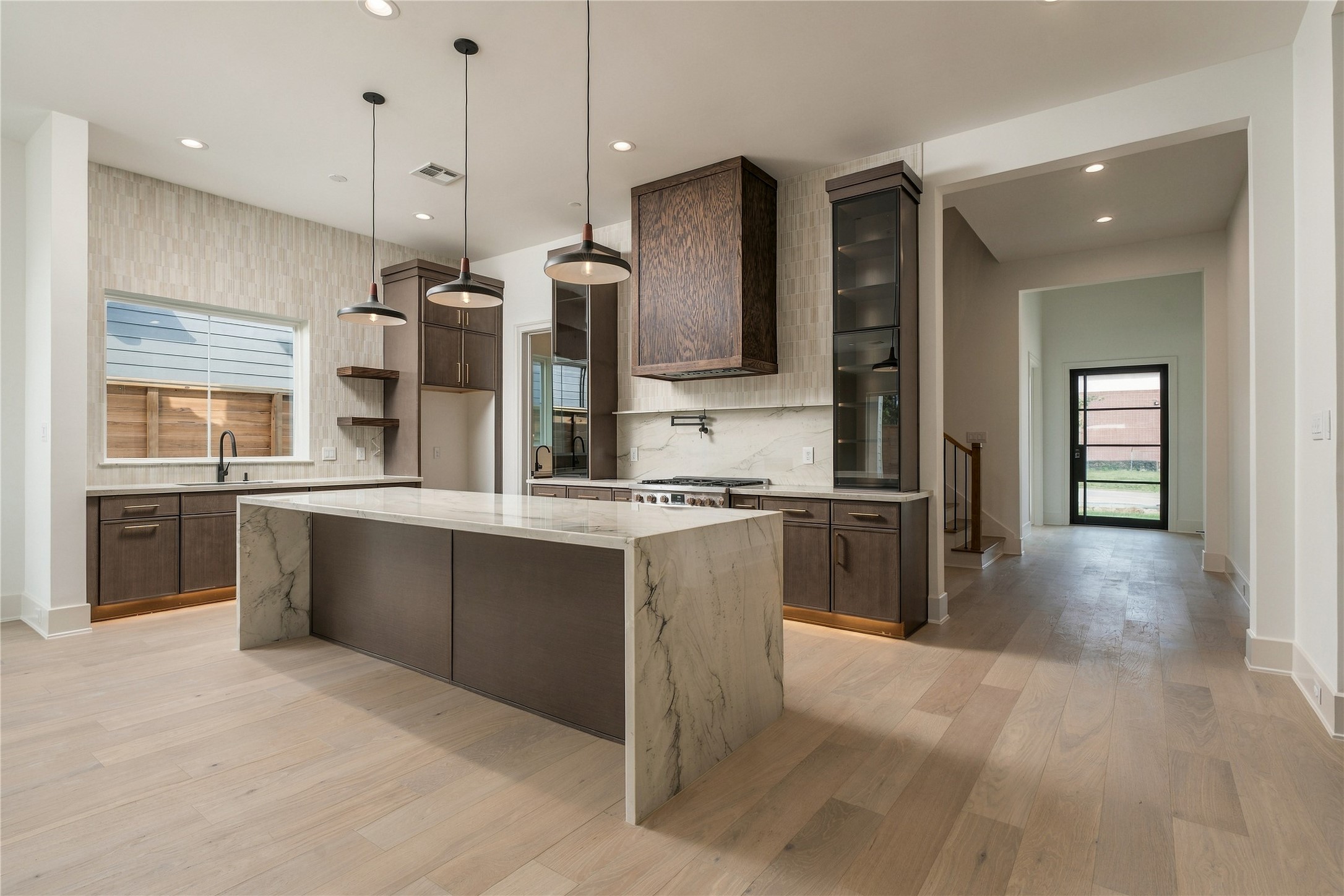 The kitchen makes an immediate statement with imported Mount Blanc Quartzite, custom cabinetry, and a dramatic oversized island, creating a natural centerpiece for both everyday living and entertaining.