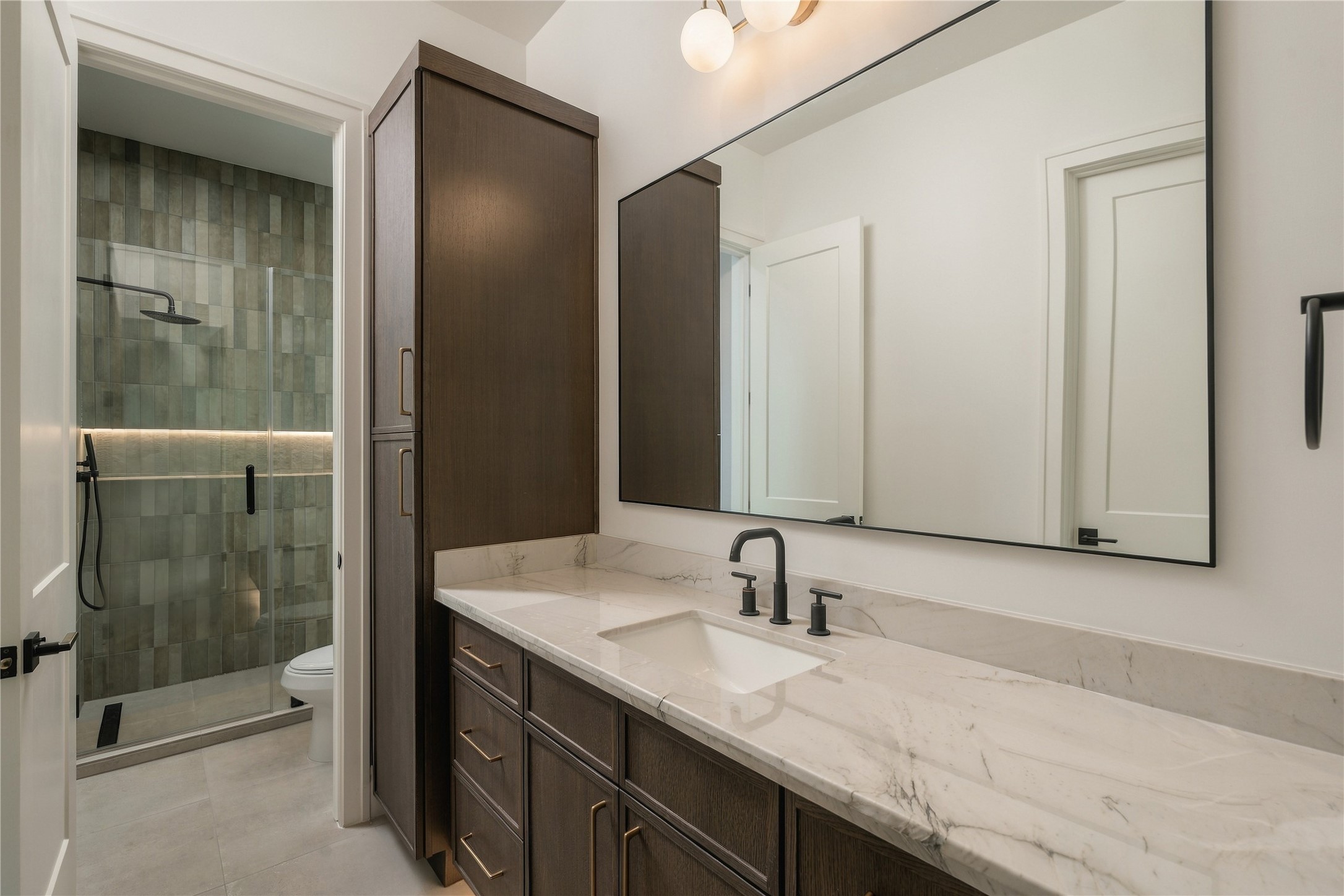 The secondary bath is finished with Mount Blanc Quartzite countertops, full-height designer tile, and a frameless glass shower, bringing the same level of finish found throughout the home into the guest accommodations.