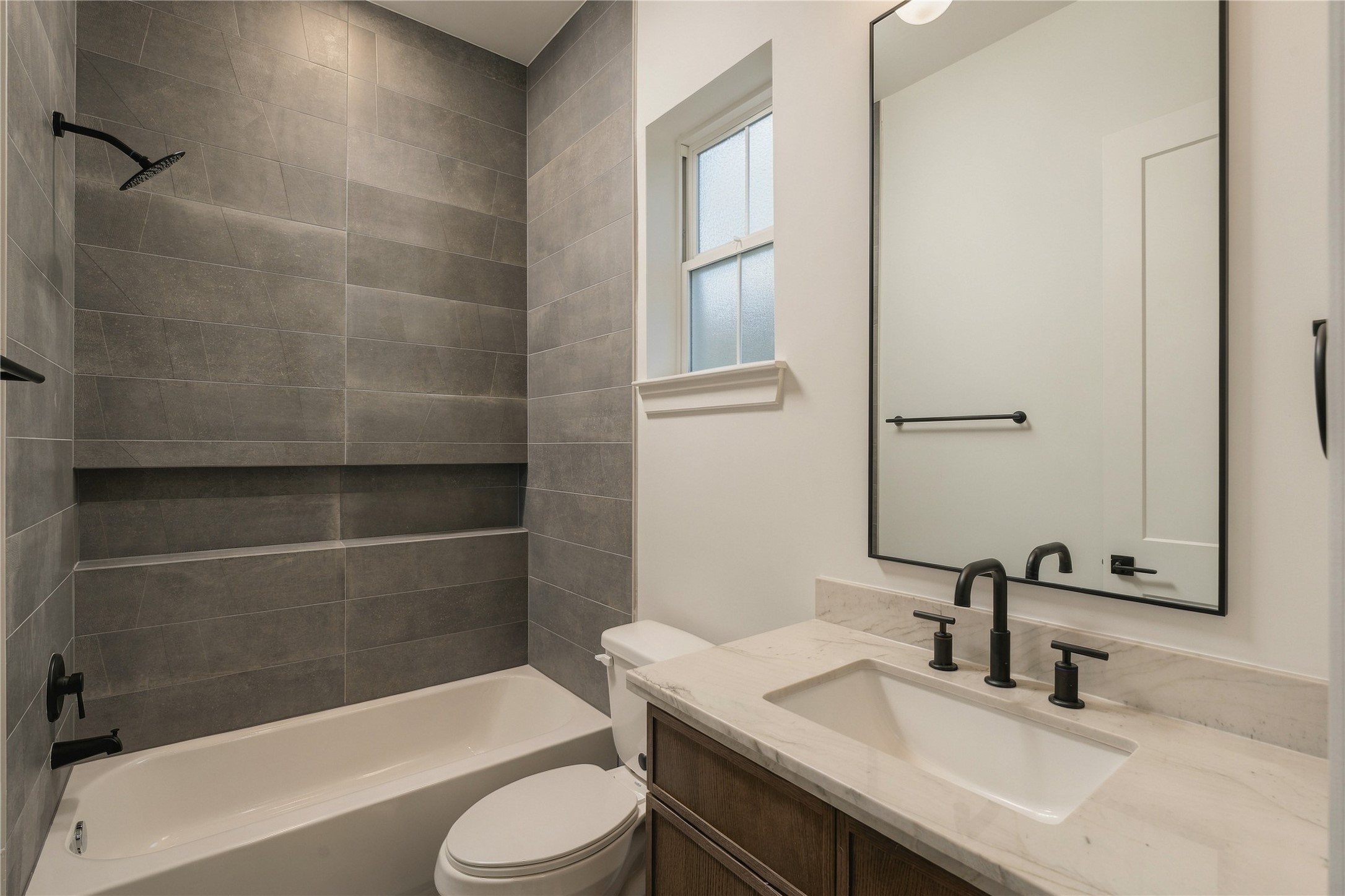 A well-appointed secondary bath features a frameless glass shower, full-height designer tile, and a shower niche, continuing the homes attention to detail across every ensuite.