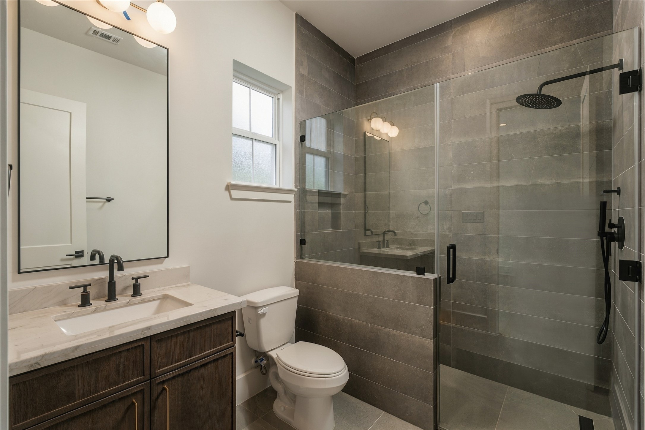 This secondary bath pairs Mount Blanc Quartzite with full-height designer tile and a frameless glass shower, creating a polished ensuite experience with finishes typically reserved for a primary suite.