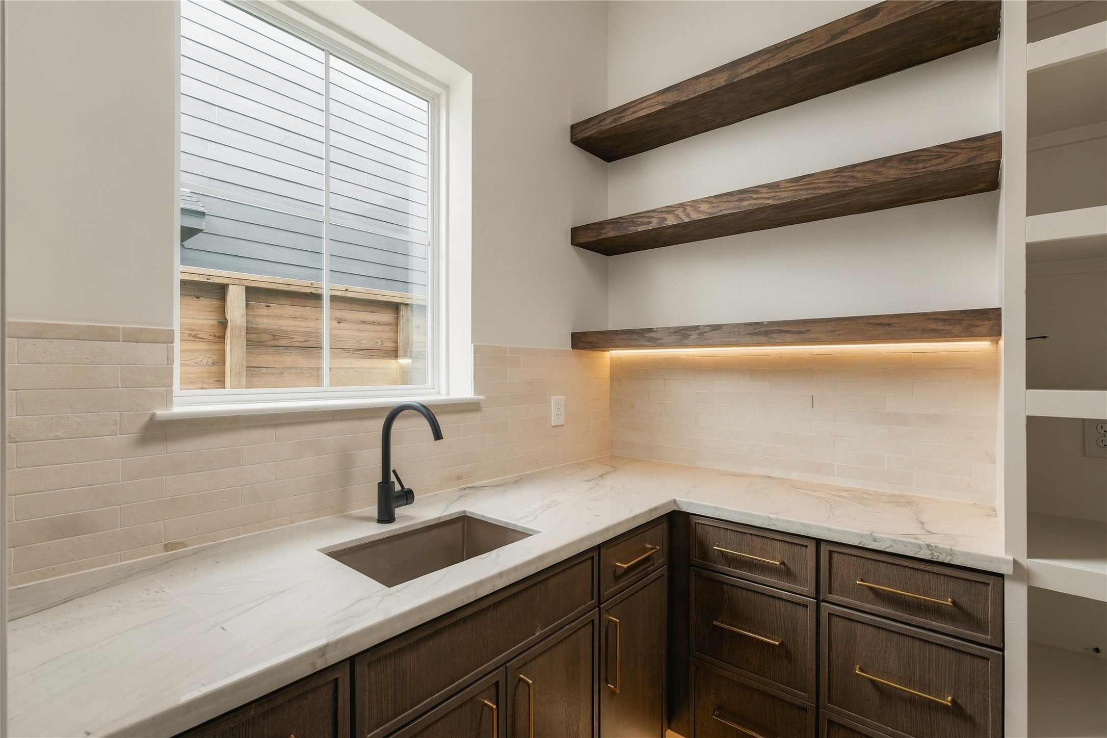 A discreet scullery-style pantry extends the kitchens functionality with generous prep space, additional cabinetry, open white oak shelving, and its own sinkkeeping the main kitchen ready for entertaining.
