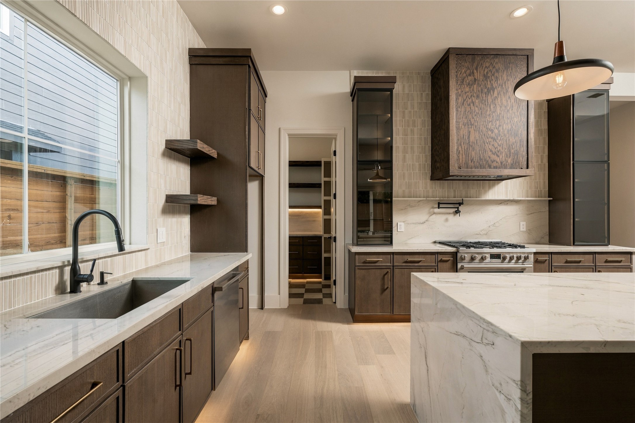 A closer view reveals the kitchens layered craftsmanship, where custom white oak details, glass-front cabinetry, and integrated LED lighting bring warmth and dimension to the space.