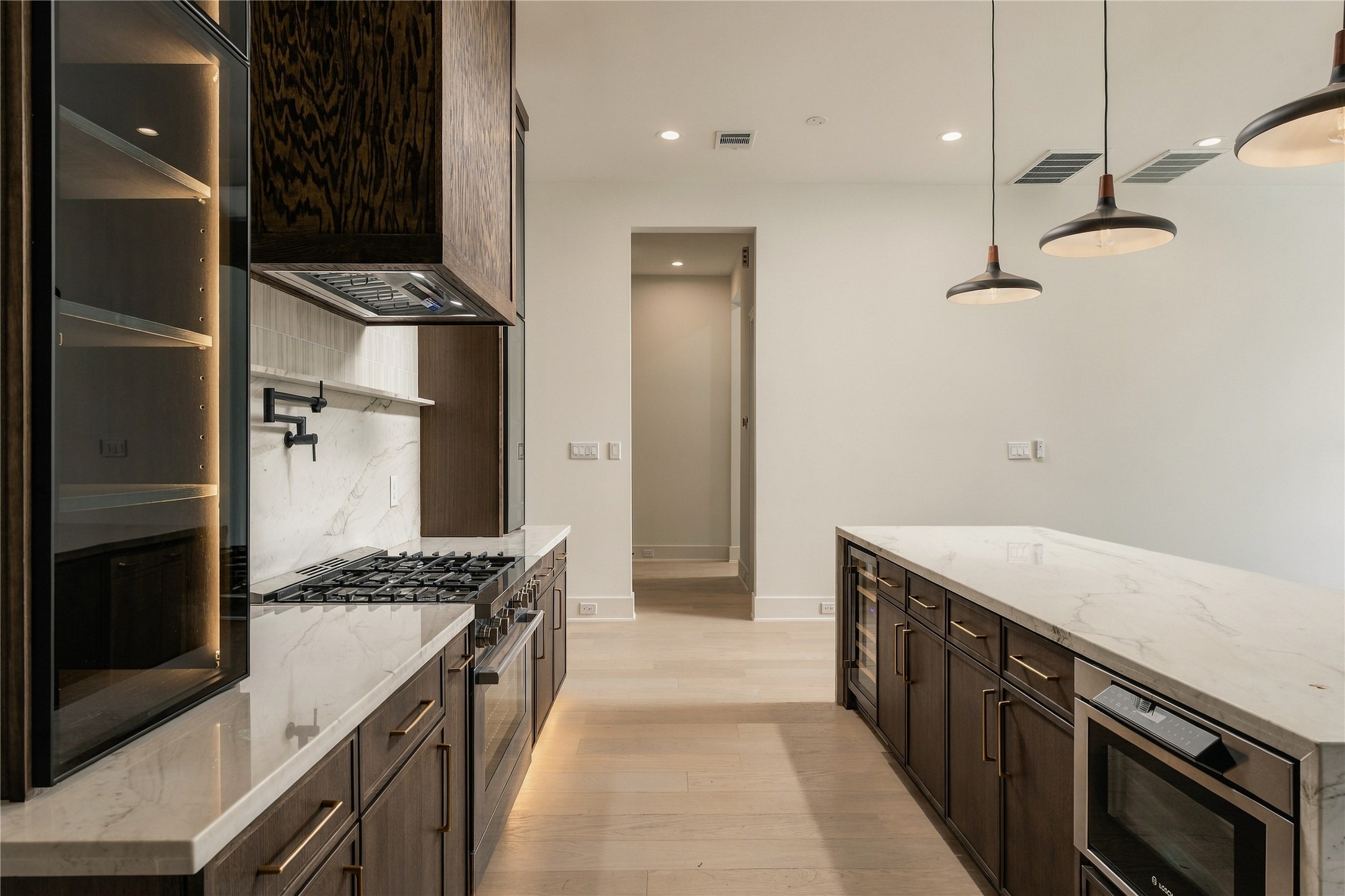 A dramatic perspective showcases the kitchens Midnight Glass Towers and illuminated cabinetry, creating a striking contrast against the warmth of the white oak finishes
