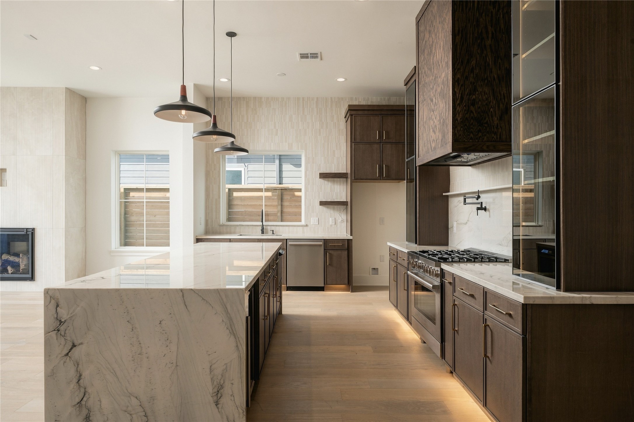 Custom Midnight Glass Towers frame the Bosch range, complemented by a white oak vent hood and illuminated cabinetry that gives the kitchen a distinctly tailored, furniture-like quality.