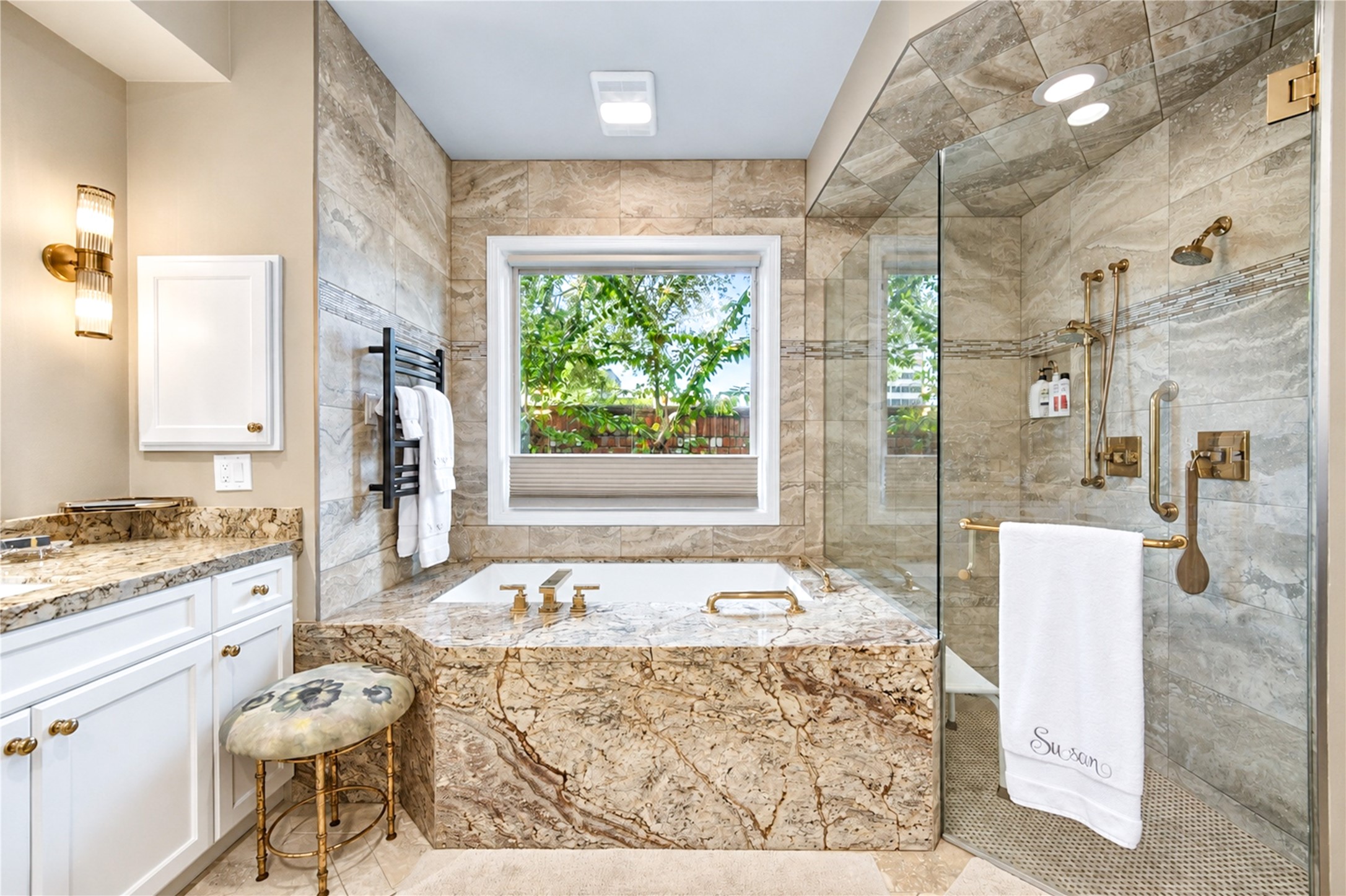 The first-floor primary bath showcases a granite-clad air-jet tub, a frameless glass shower, a towel warmer and a window overlooking greenery.