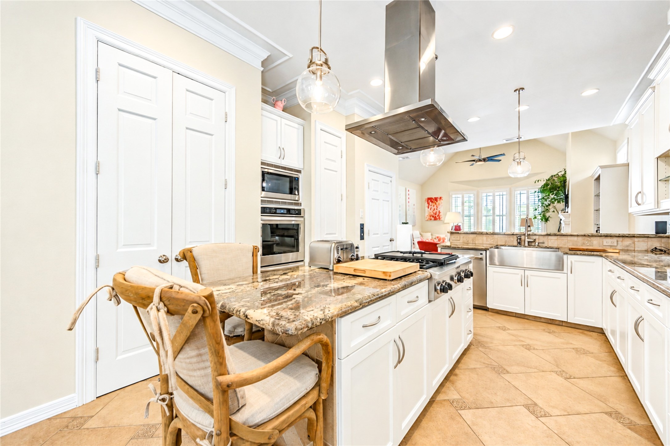 The island cooktop, stainless hood and white cabinetry open to a vaulted family area filled with light from a wall of windows.