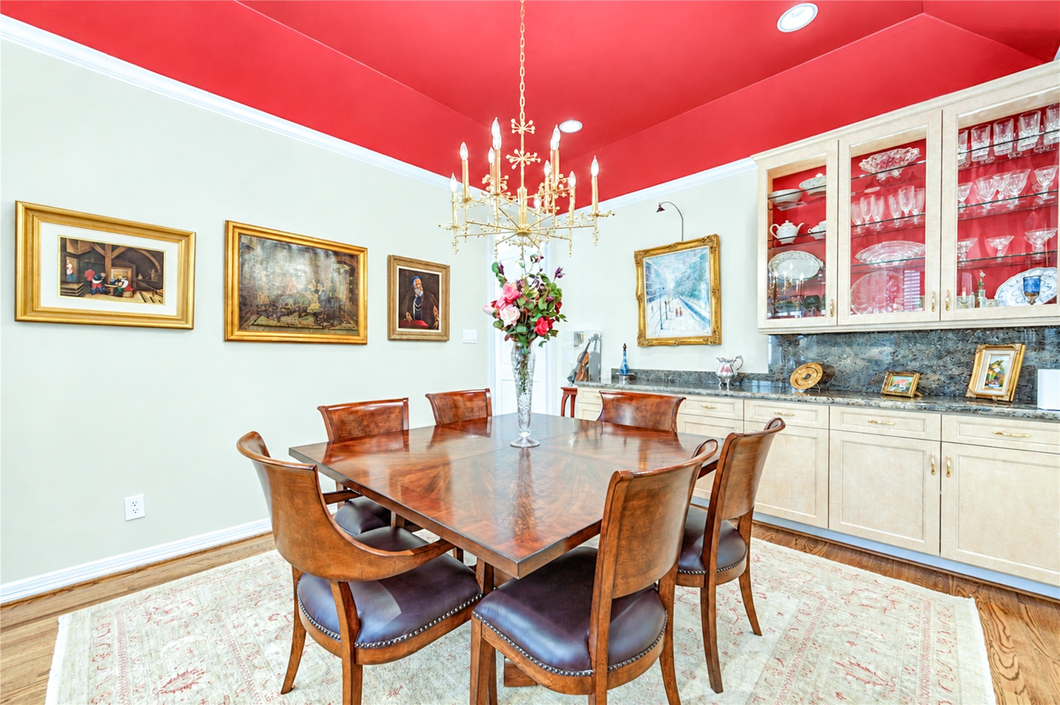 Glass-front built-in cabinetry and a granite-topped buffet line the dining room wall beneath crown molding.