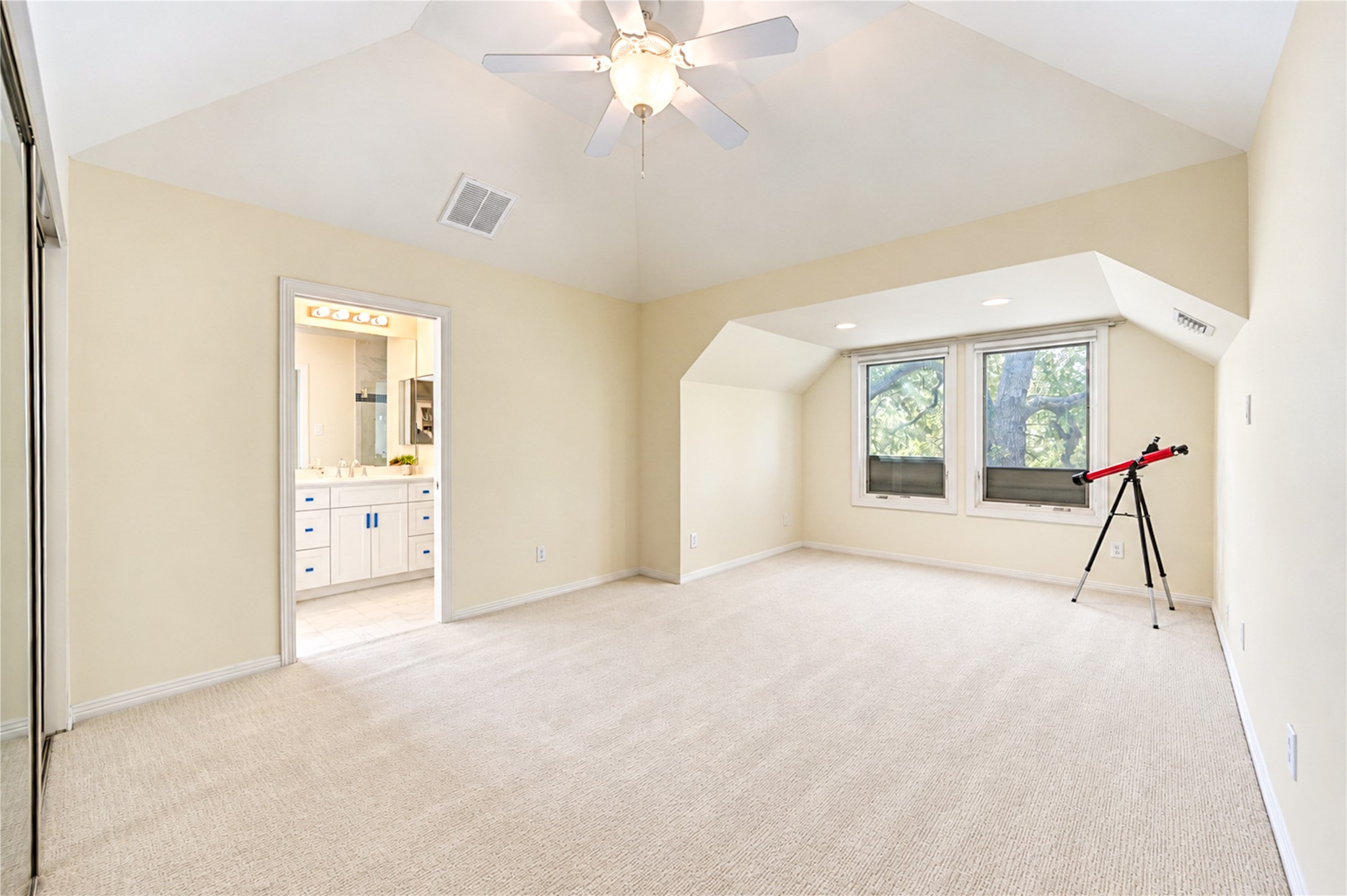 A bright third-floor bedroom features a vaulted ceiling, a ceiling fan, tall windows and direct access to a bath.