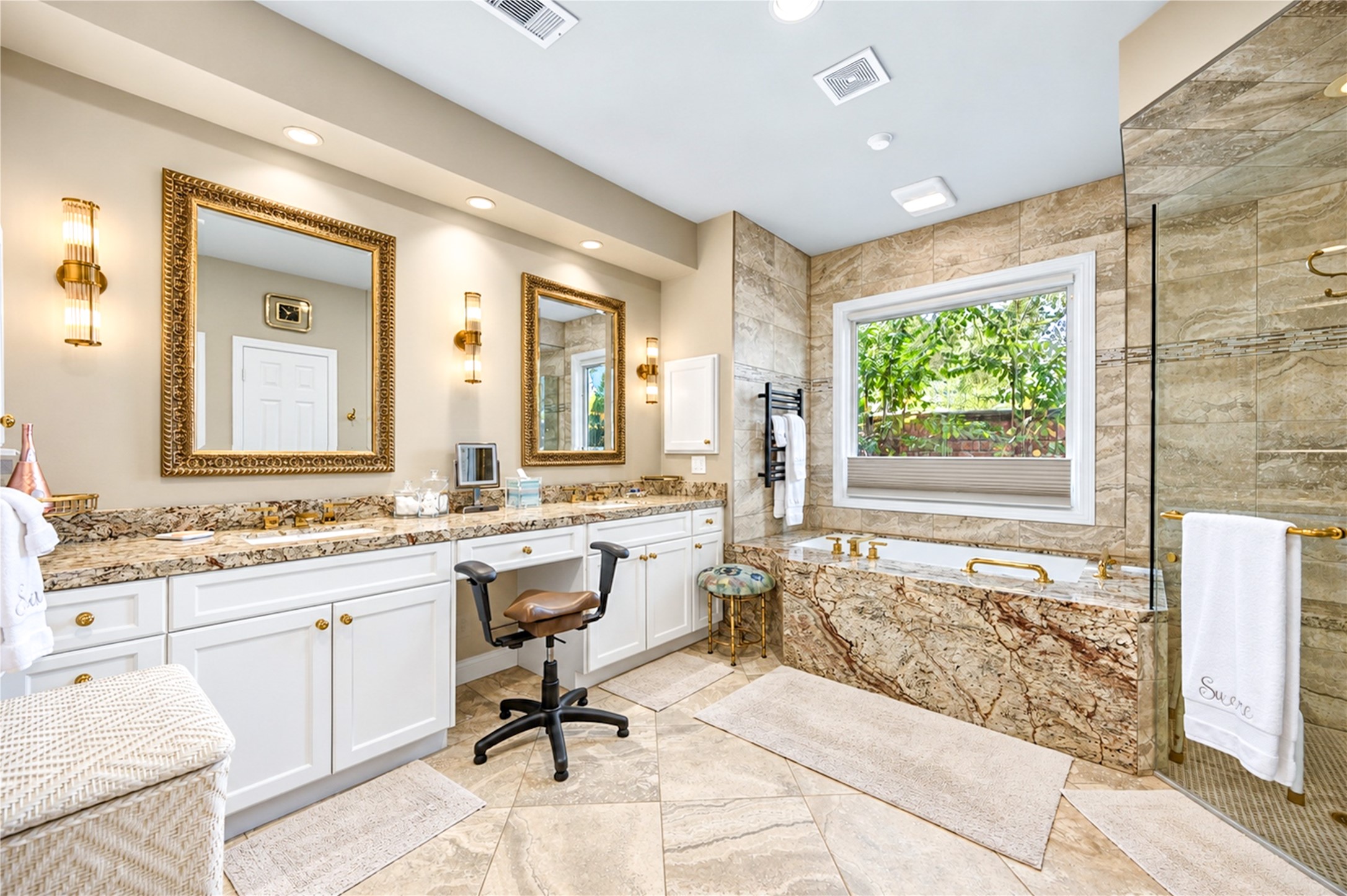 Dual sinks, granite countertops and a built-in vanity seating area complete the primary bath beneath gold-framed mirrors.