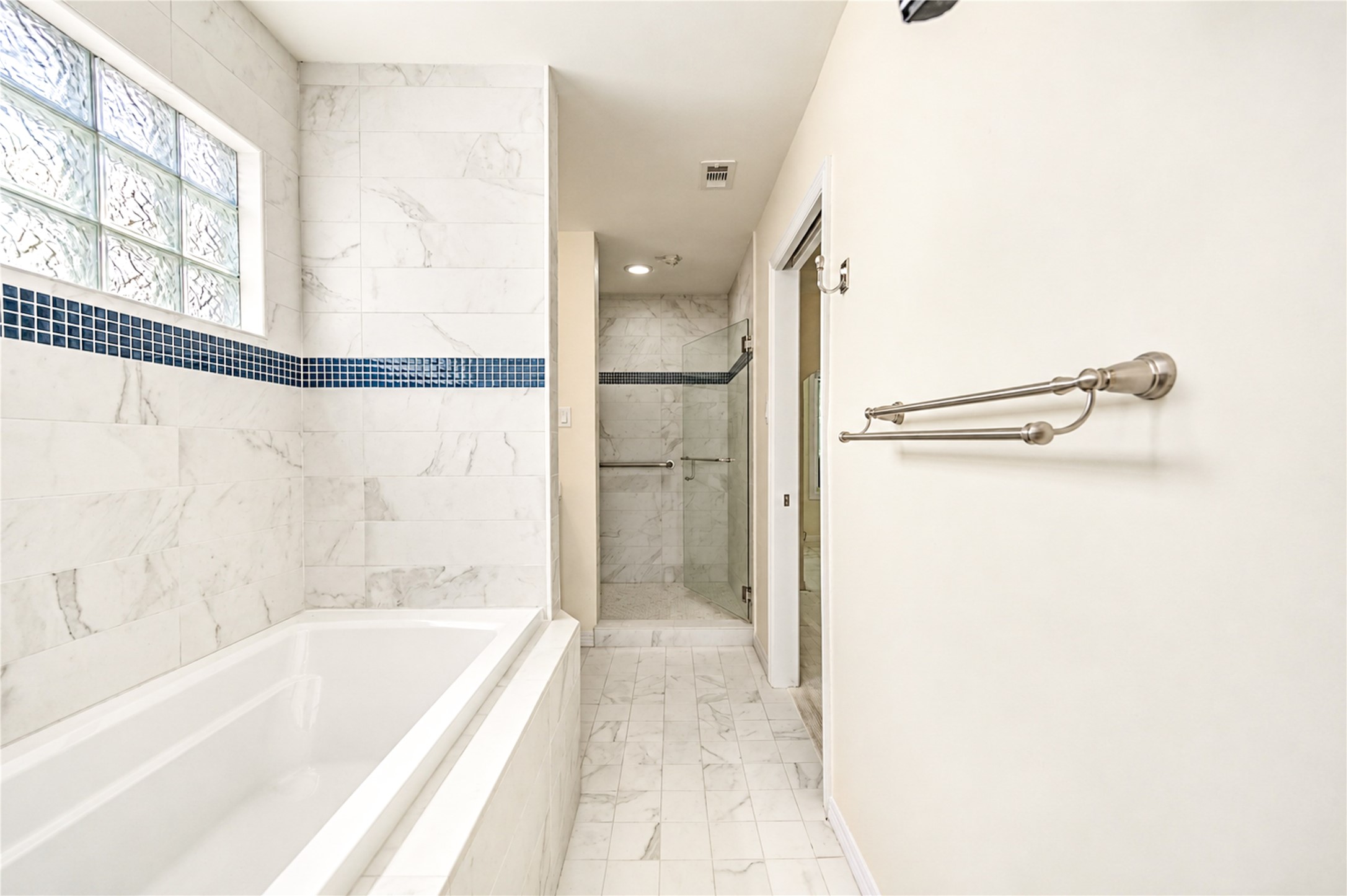 A soaking tub and a glass-enclosed shower are set against marble-look tile and a glass-block window in this third-floor bath.