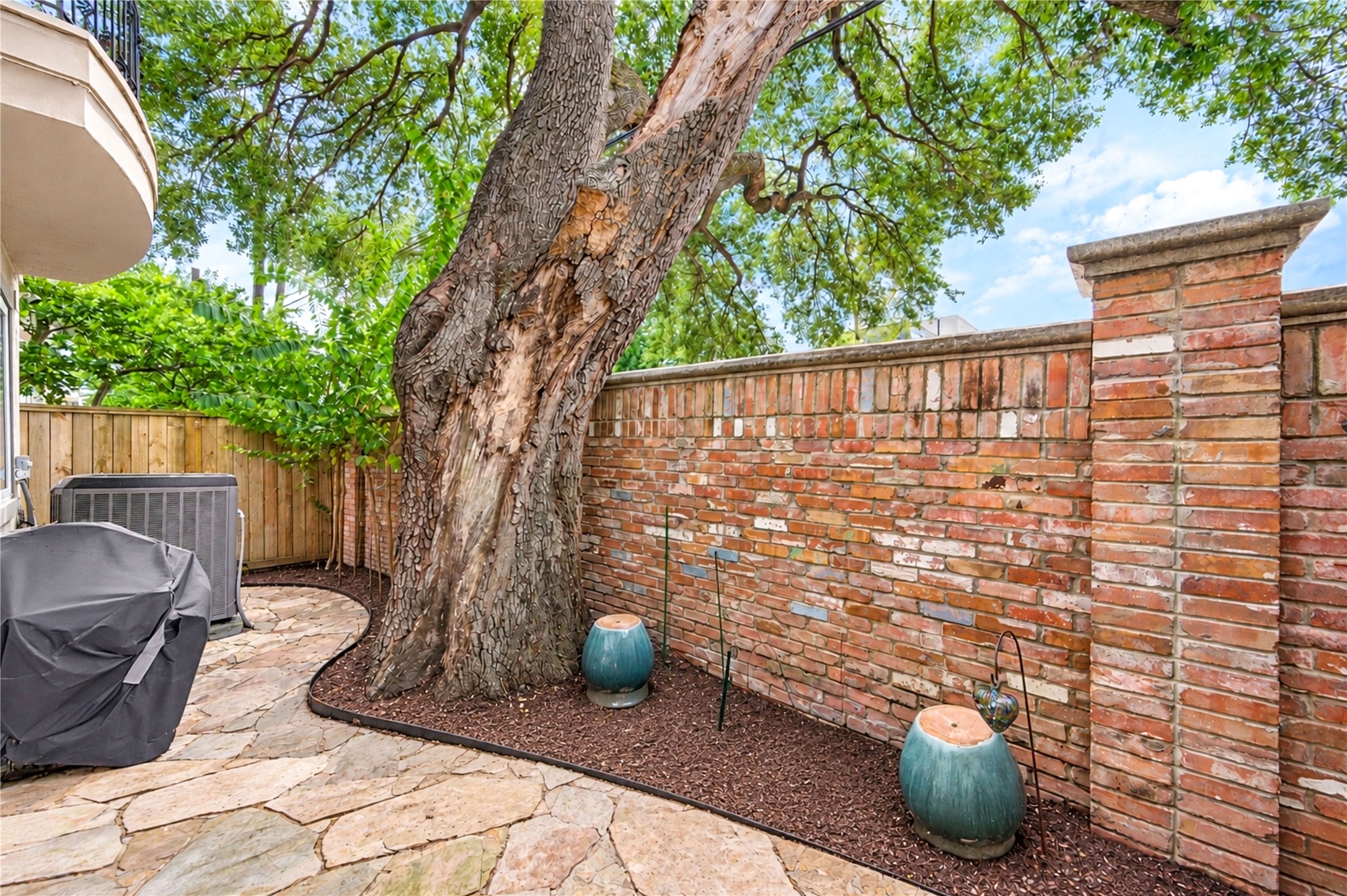 A flagstone patio beneath a mature oak is enclosed by a brick wall, creating a private outdoor retreat.