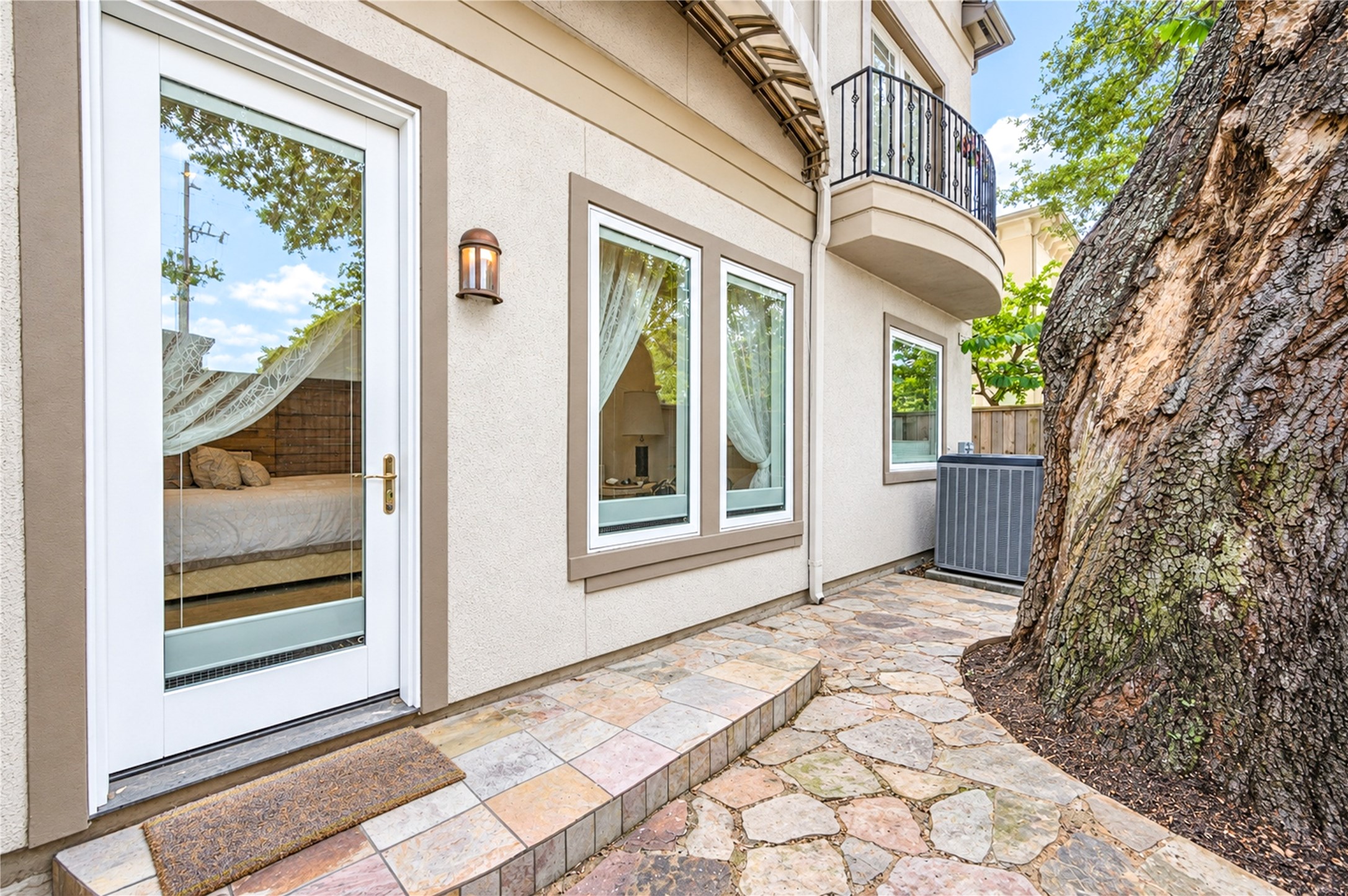 Flagstone paving leads past a mature oak to a glass-paneled door at the side of the home, with a balcony above.