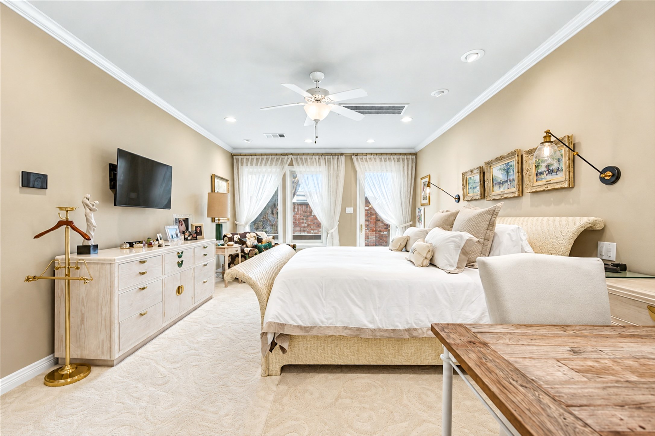 Large windows along one wall bring natural light into the first-floor primary bedroom, beneath a ceiling fan and recessed lighting.