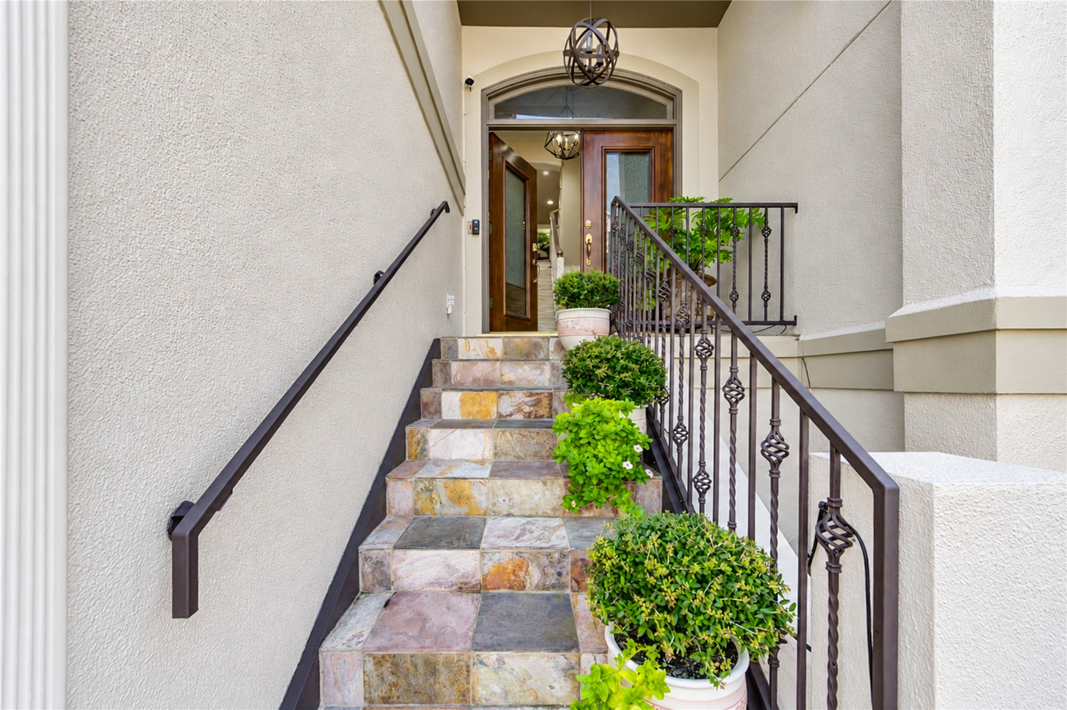 A slate-clad stair with a wrought-iron railing and lush plantings leads to the arched, glass-paneled front door. A slate-clad stair with a wrought-iron railing and lush plantings leads to the arched, glass-paneled front door.