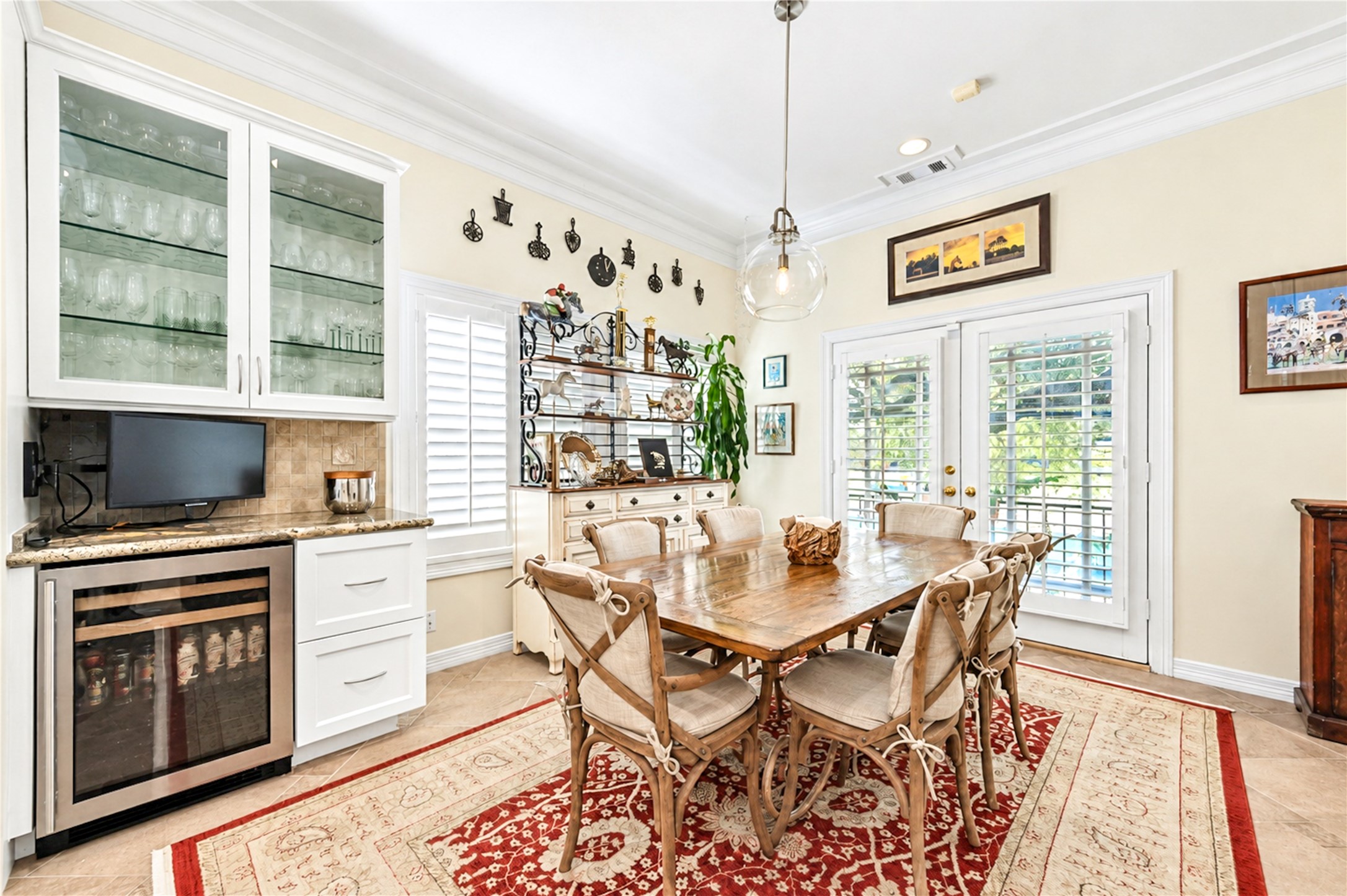 A glass-front cabinet wall, a granite counter and a wine refrigerator sit beside French doors that bring natural light into the breakfast area.