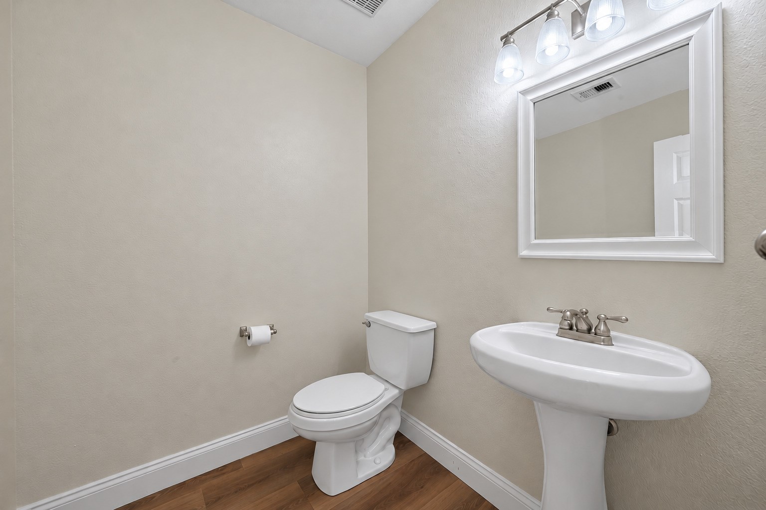 A pedestal sink, well-lit mirror, and streamlined fixtures give this main-level powder room a neat, uncluttered finish, offering a practical stop for guests.