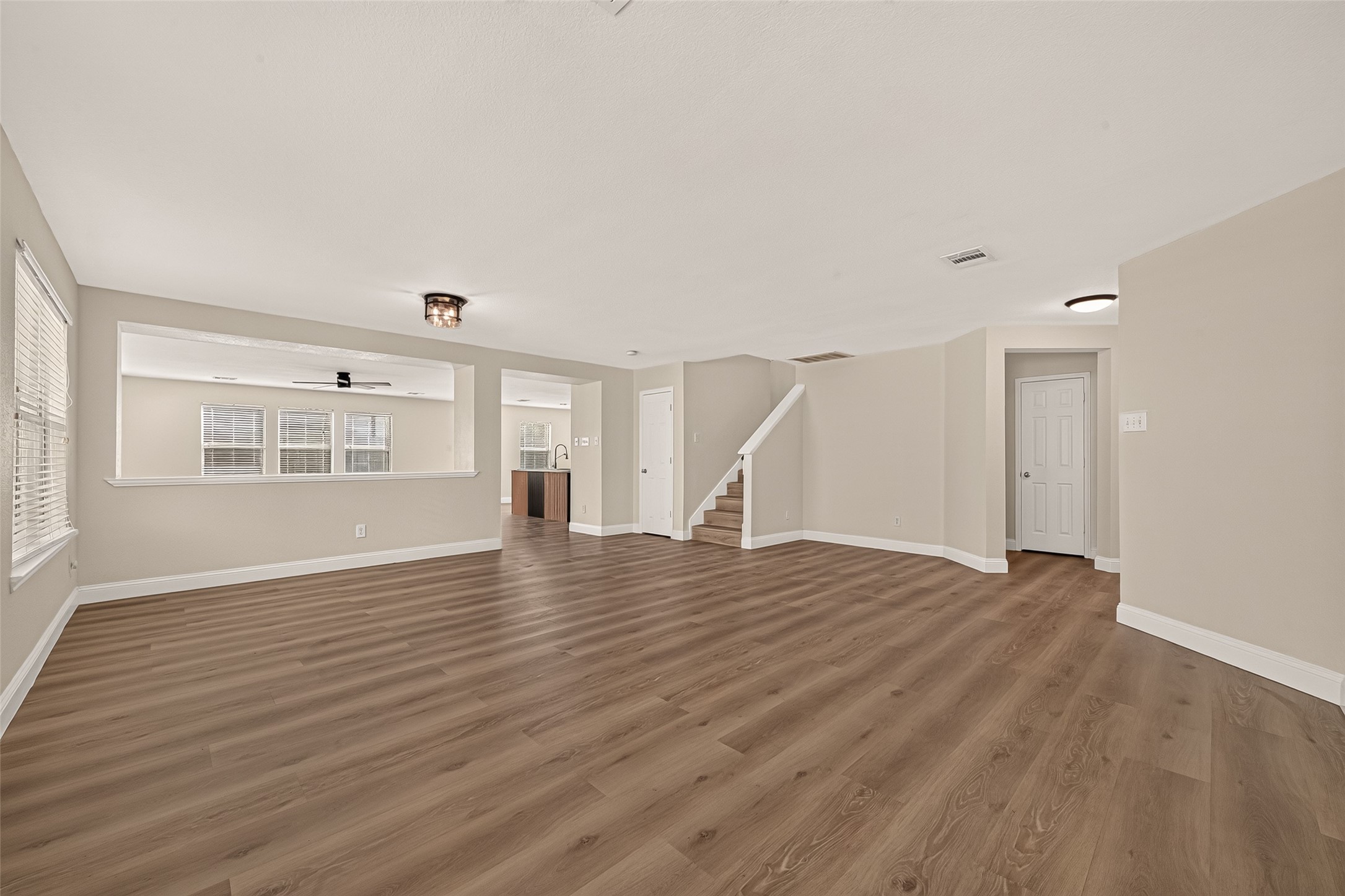 An expansive, open space offers the flexibility to create distinct living and dining arrangements. Natural light pours through the large windows, highlighting the warm wood-look flooring and providing a bright foundation for a variety of furniture layouts.