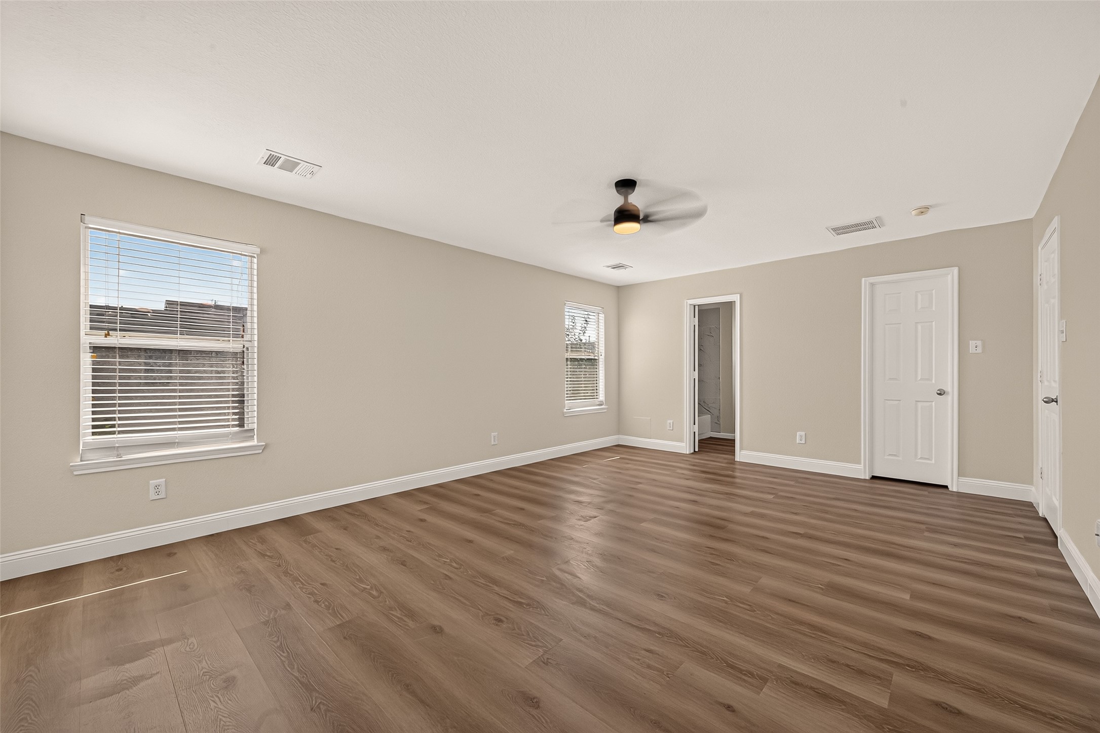 Large windows brighten this expansive bedroom, giving the room an airy quality throughout the day. A ceiling fan adds comfort, while the ample floor space leaves plenty of room to arrange furnishings and create a personal haven.