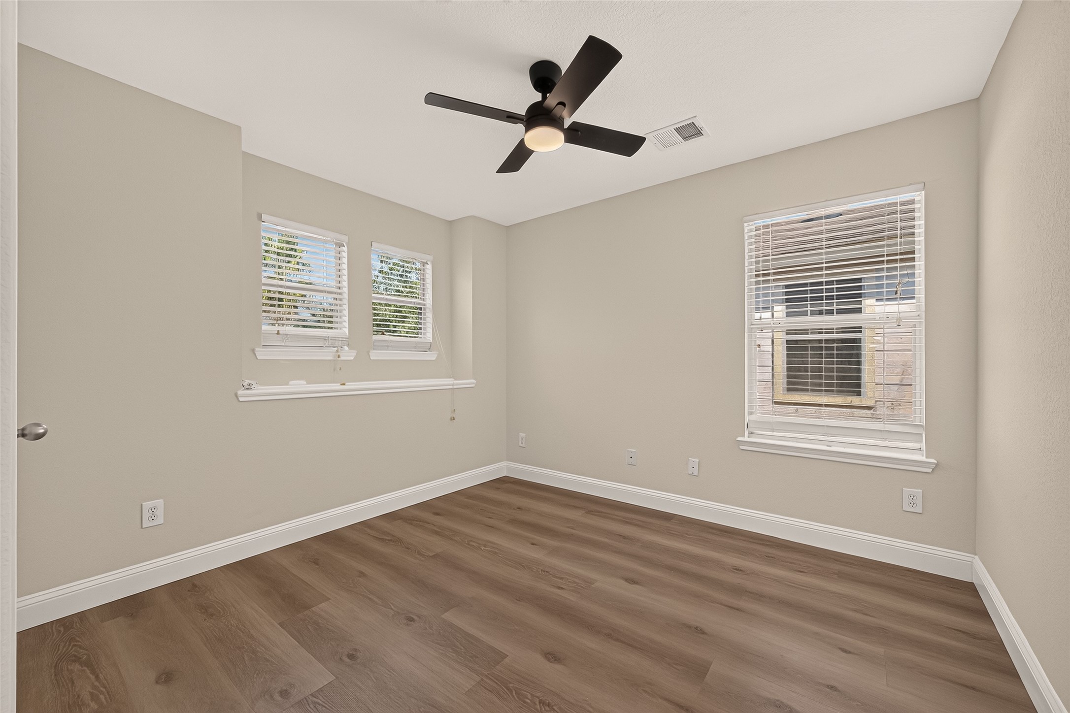 Multiple windows bring daylight into this comfortably sized bedroom, complementing the cool neutral palette and warm-toned flooring. A ceiling fan adds everyday convenience while the understated finishes allow for a range of decorating styles.