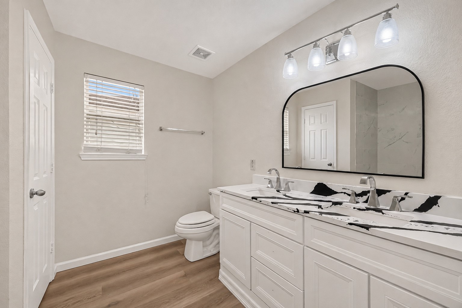 A modern dual-sink vanity offers separate preparation space, complemented by a striking countertop and a window that welcomes daylight into the primary bath.