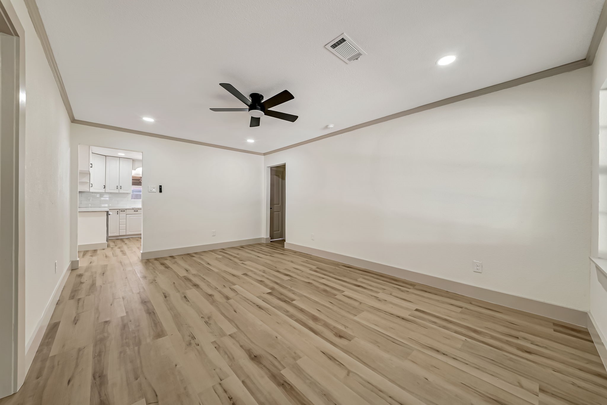 Spacious living room with elegant wood like flooring, modern ceiling fan, and recessed lighting, seamlessly connecting to a bright kitchen. Spacious living room with elegant wood like flooring, modern ceiling fan, and recessed lighting, seamlessly connecting to a bright kitchen.