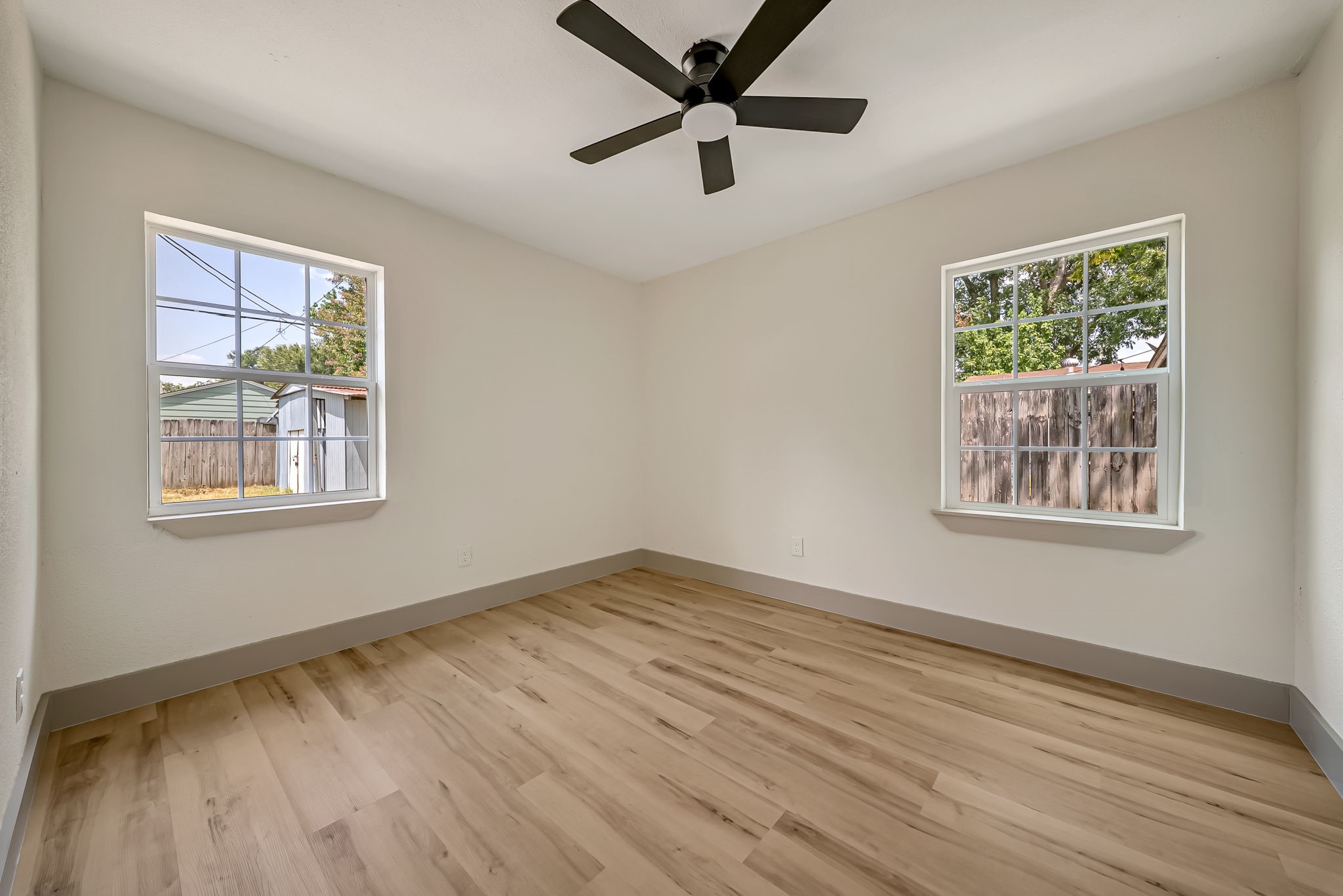 Bright and inviting bedroom featuring large windows, sleek wood flooring, and a modern ceiling fan.