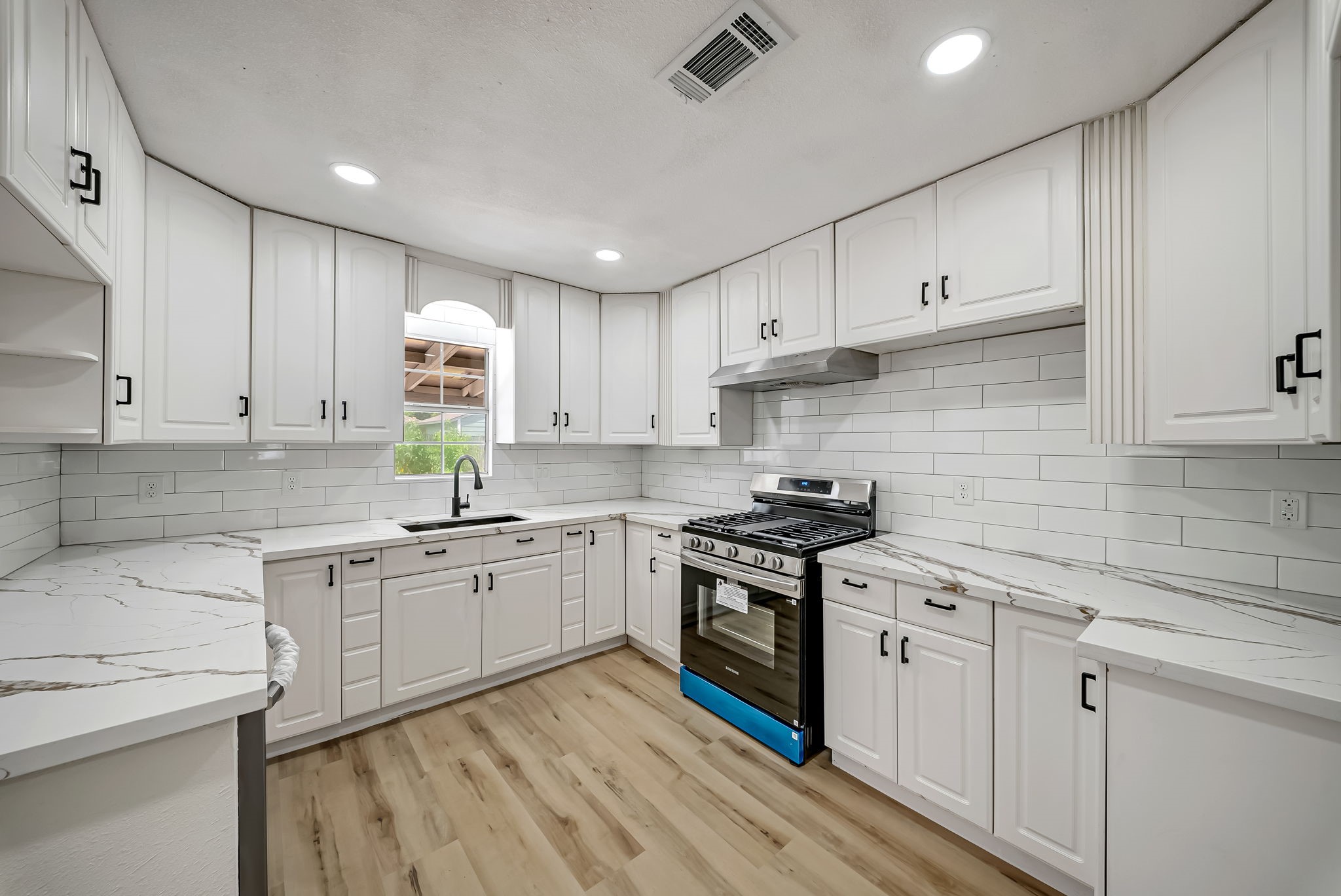 Elegant kitchen with sleek white cabinetry, modern stainless steel appliances, and stylish quartz countertops, all complemented by a chic subway tile backsplash and warm LVP flooring.