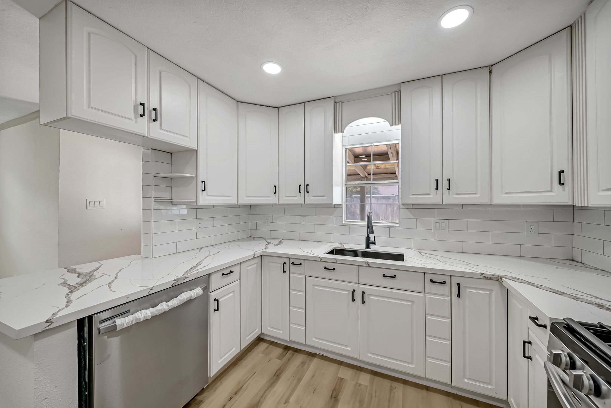 Elegant kitchen featuring pristine white cabinetry, sleek quartz countertops, and modern stainless steel appliances, complemented by a large window that invites natural light. Elegant kitchen featuring pristine white cabinetry, sleek quartz countertops, and modern stainless steel appliances, complemented by a large window that invites natural light.