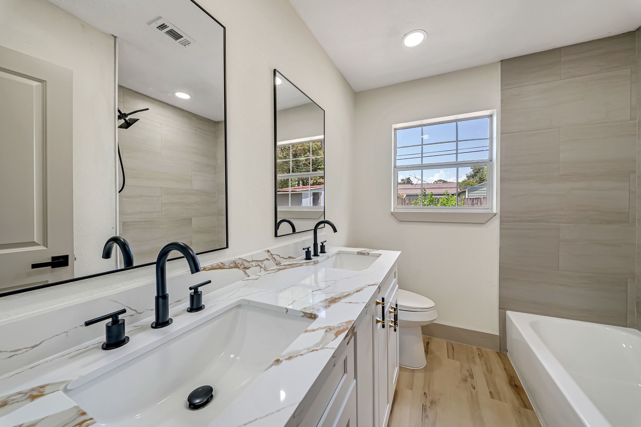Elegant bathroom featuring a dual-sink vanity with sleek black fixtures, large modern mirrors, and a stylish mix of marble and wood accents.
