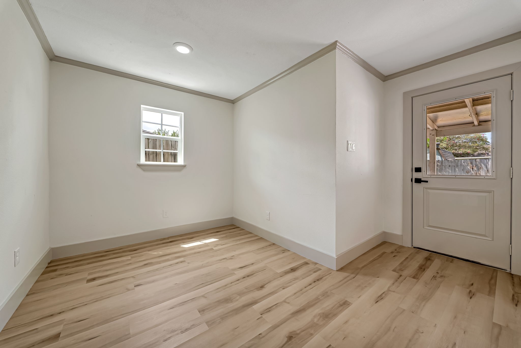 Bright and inviting room with sleek LVP floors, neutral walls, and a door leading to an outdoor space.