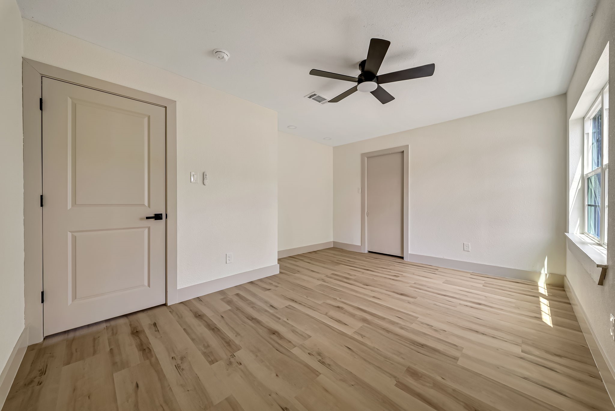 Spacious and bright room featuring sleek LVP flooring, a modern ceiling fan, and abundant natural light streaming through a large window.