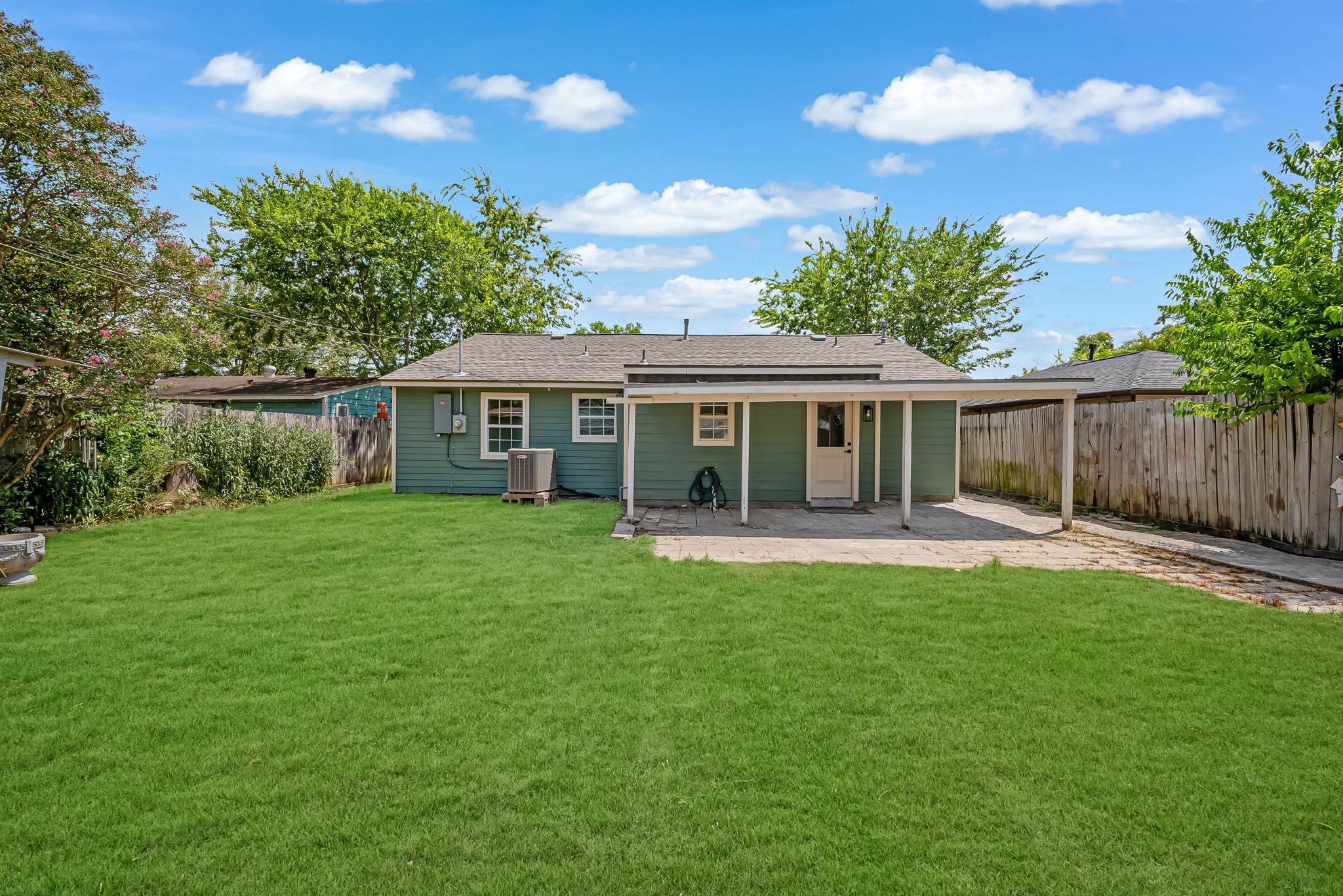 Charming backyard with a spacious lawn, cozy covered patio, and privacy fencing, perfect for outdoor relaxation and gatherings.