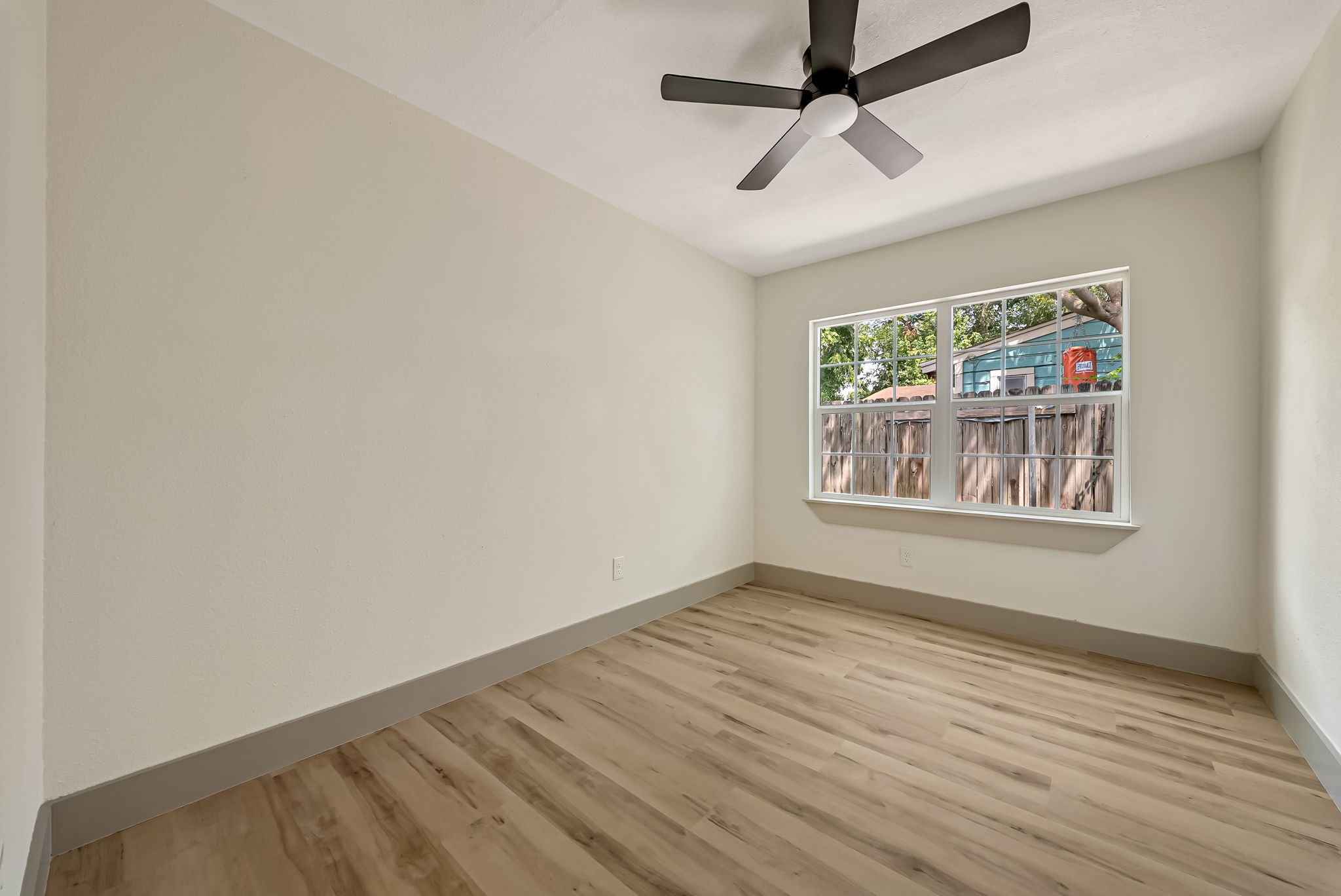 Bright bedroom featuring a large window, sleek ceiling fan, and elegant wood flooring.
