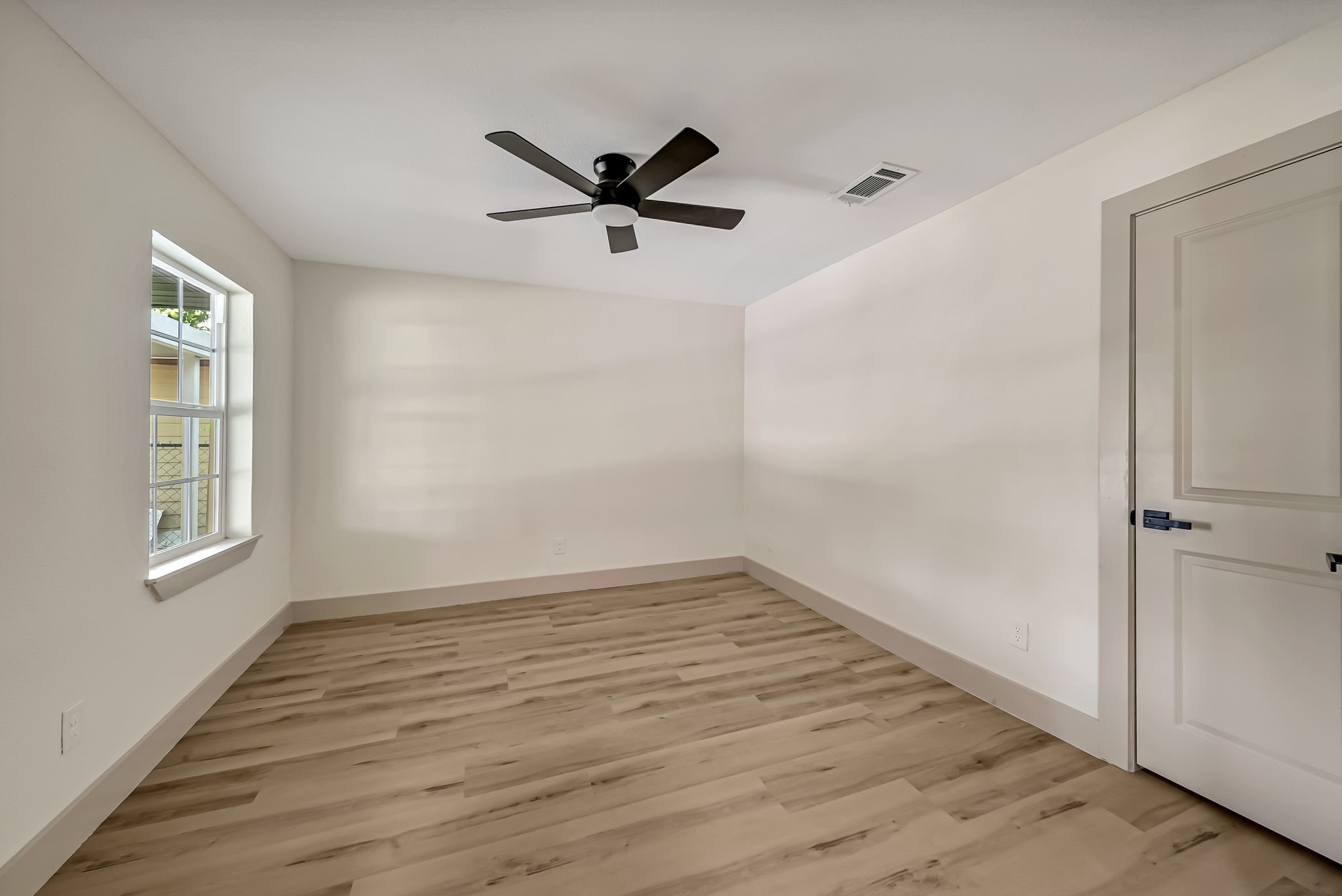 Bright and spacious office/possible bedroom room featuring sleek wood like LVP flooring, a modern ceiling fan, and ample natural light from a large window.